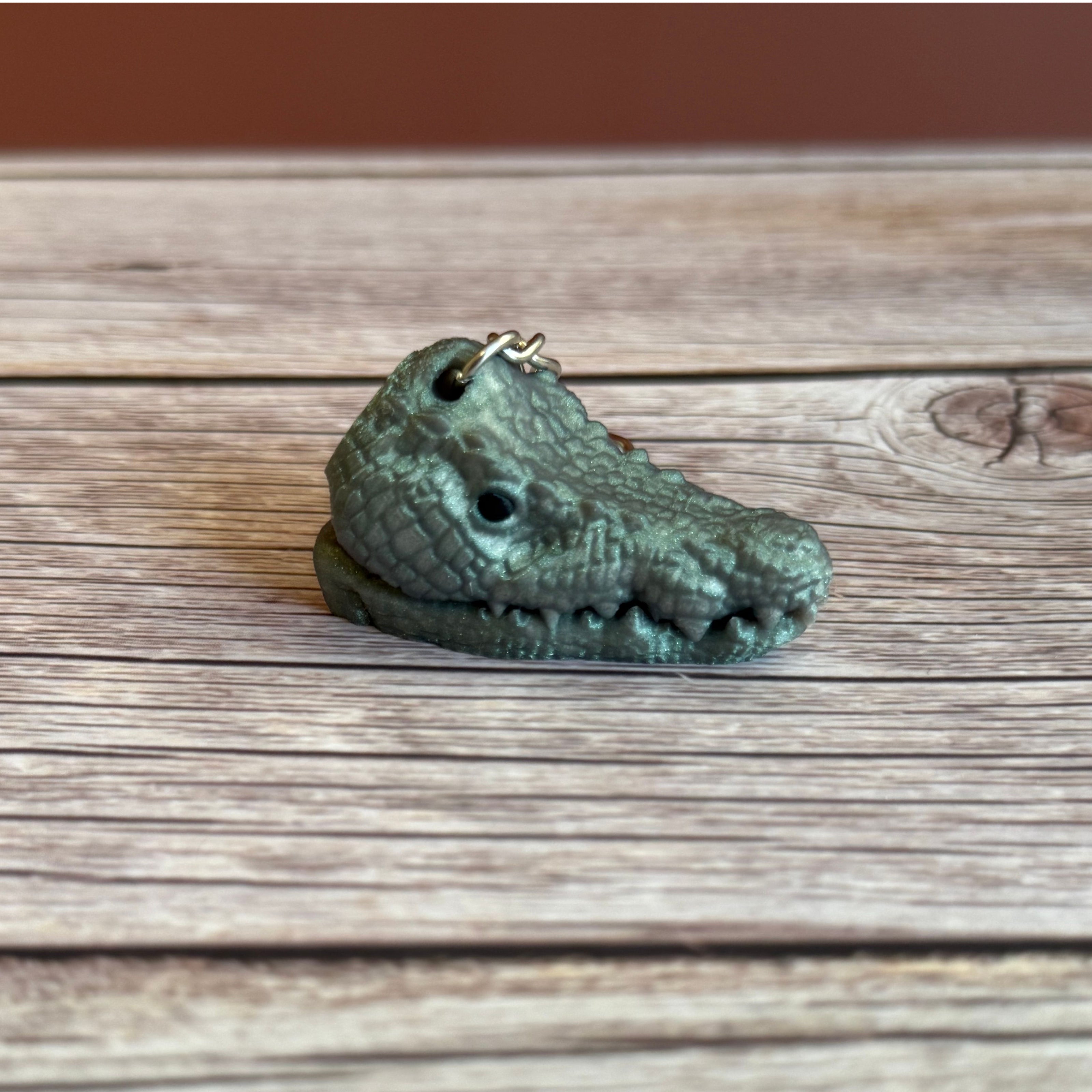 3D printed shimmer green crocodile head-shaped keychain with a closed mouth on a wooden surface