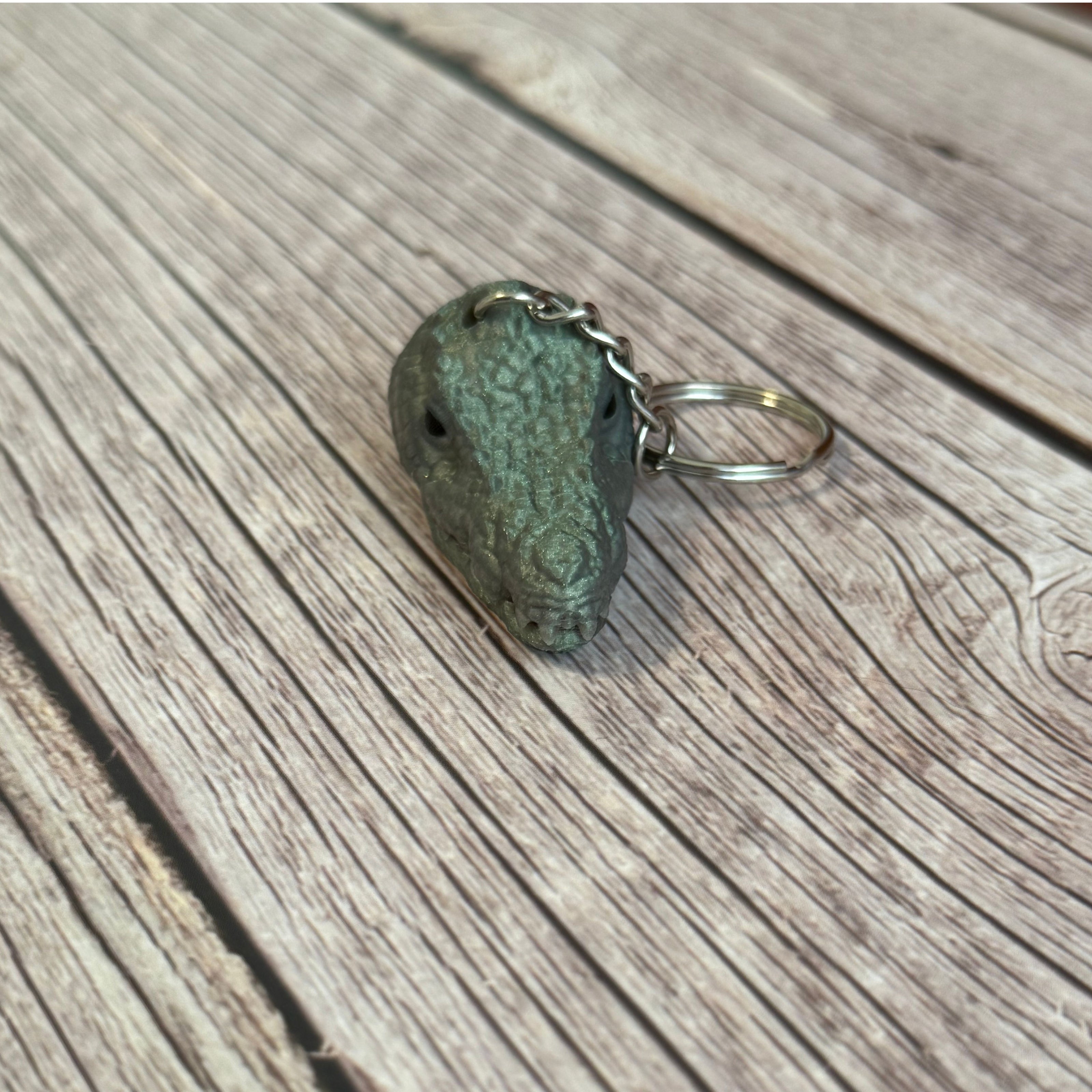 3D printed shimmer green crocodile head-shaped keychain with a closed mouth on a wooden surface