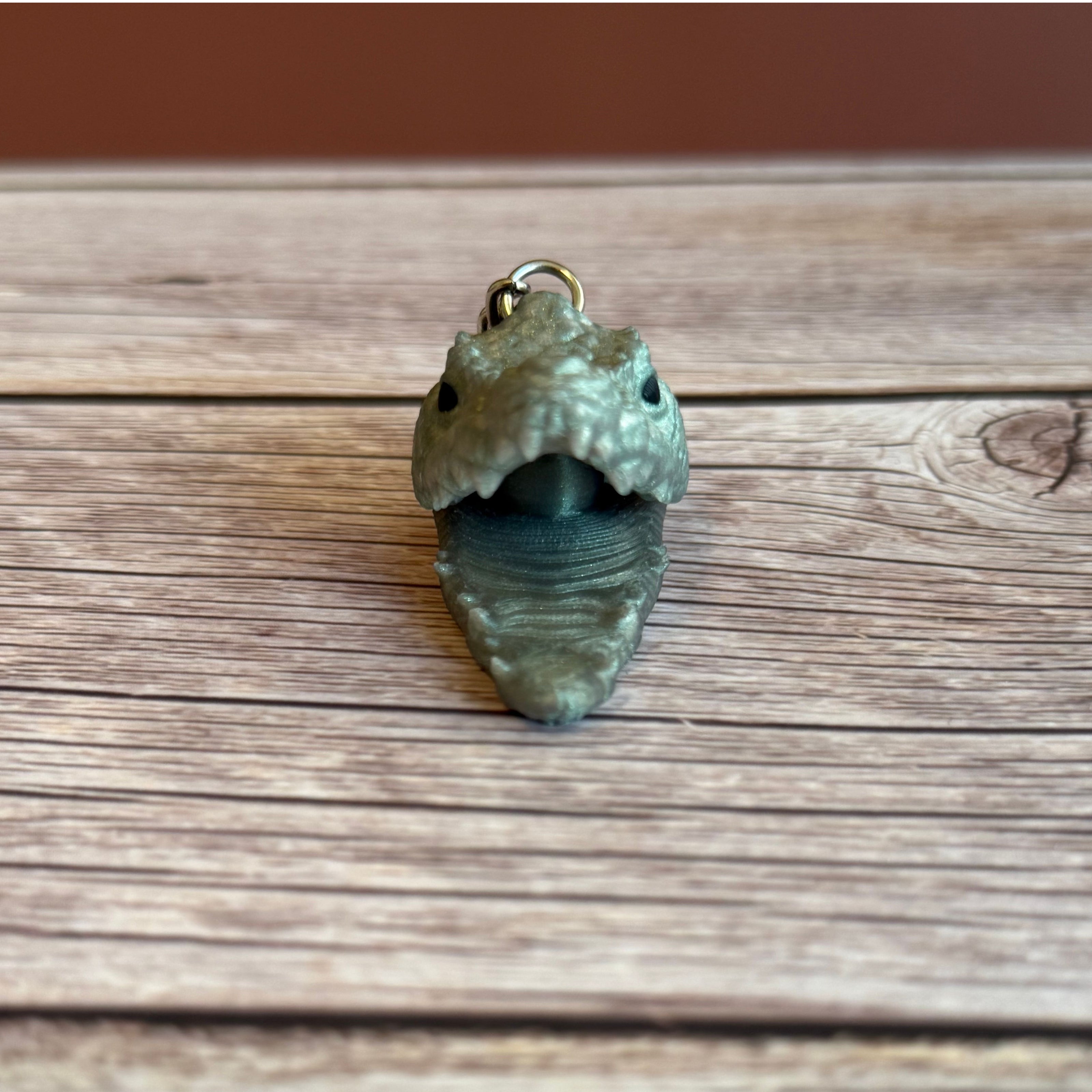 3D printed shimmer green crocodile head-shaped keychain with an open mouth on a wooden surface
