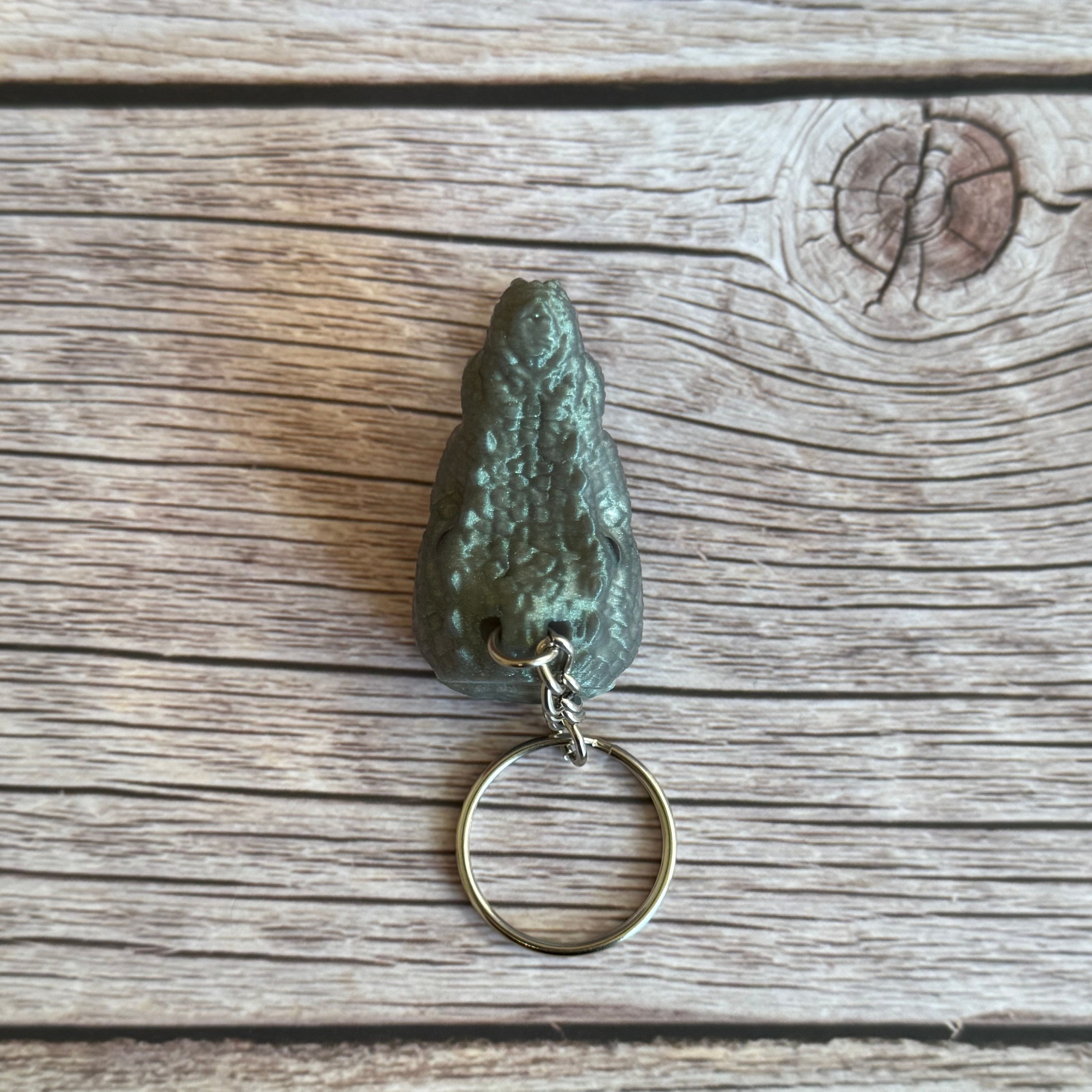 Top of a 3D printed shimmer green crocodile head-shaped keychain on a wooden surface