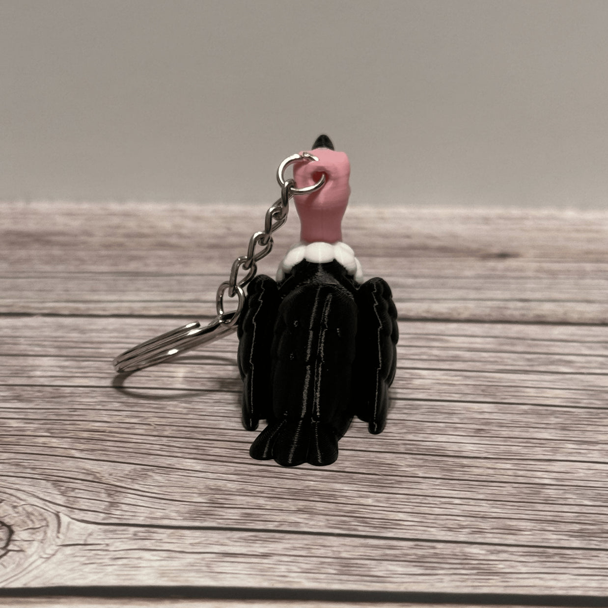 Back side of a keychain shaped like a cartoon vulture on a wooden surface 