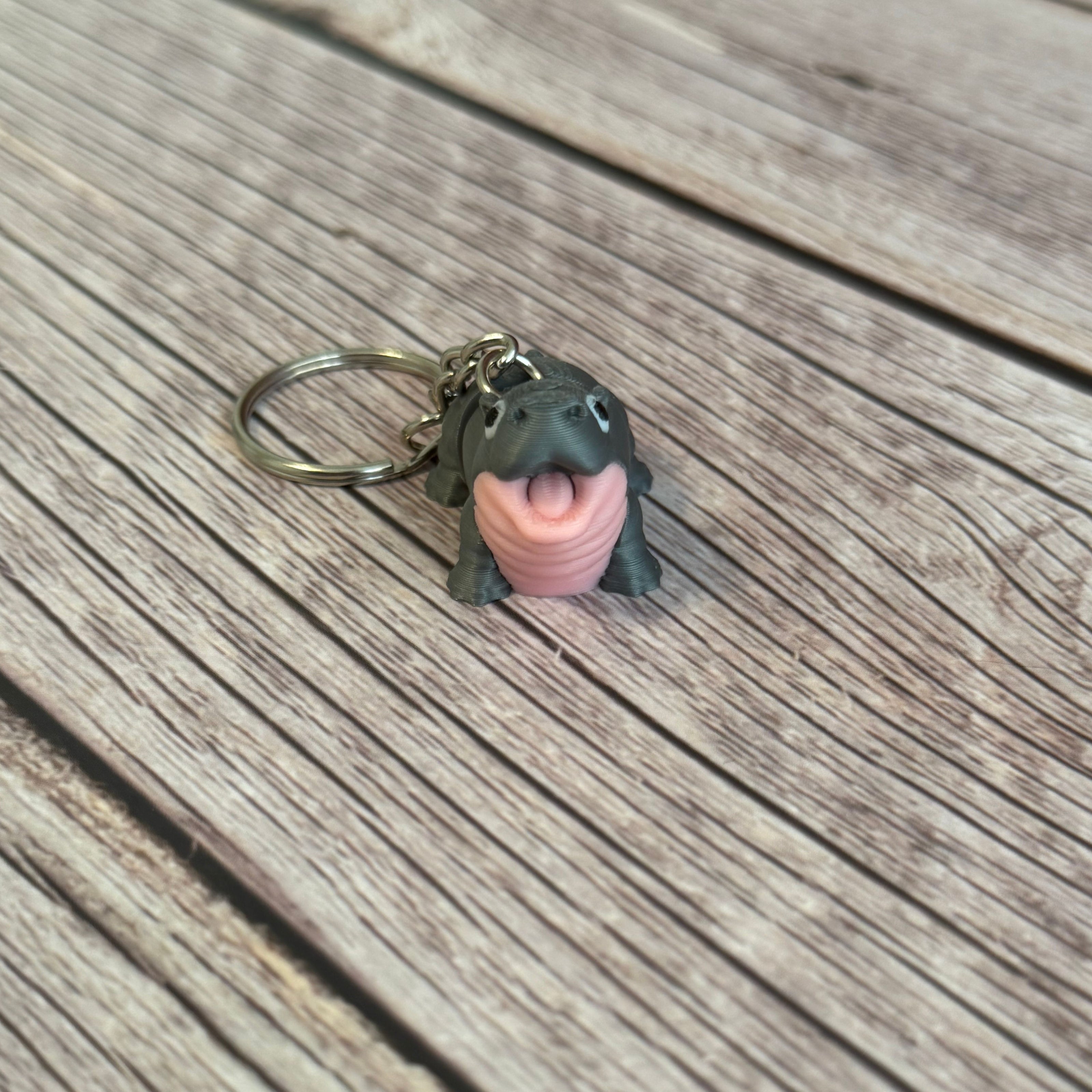 3D printed gray and pink hippo-shaped keychain on a wooden surface