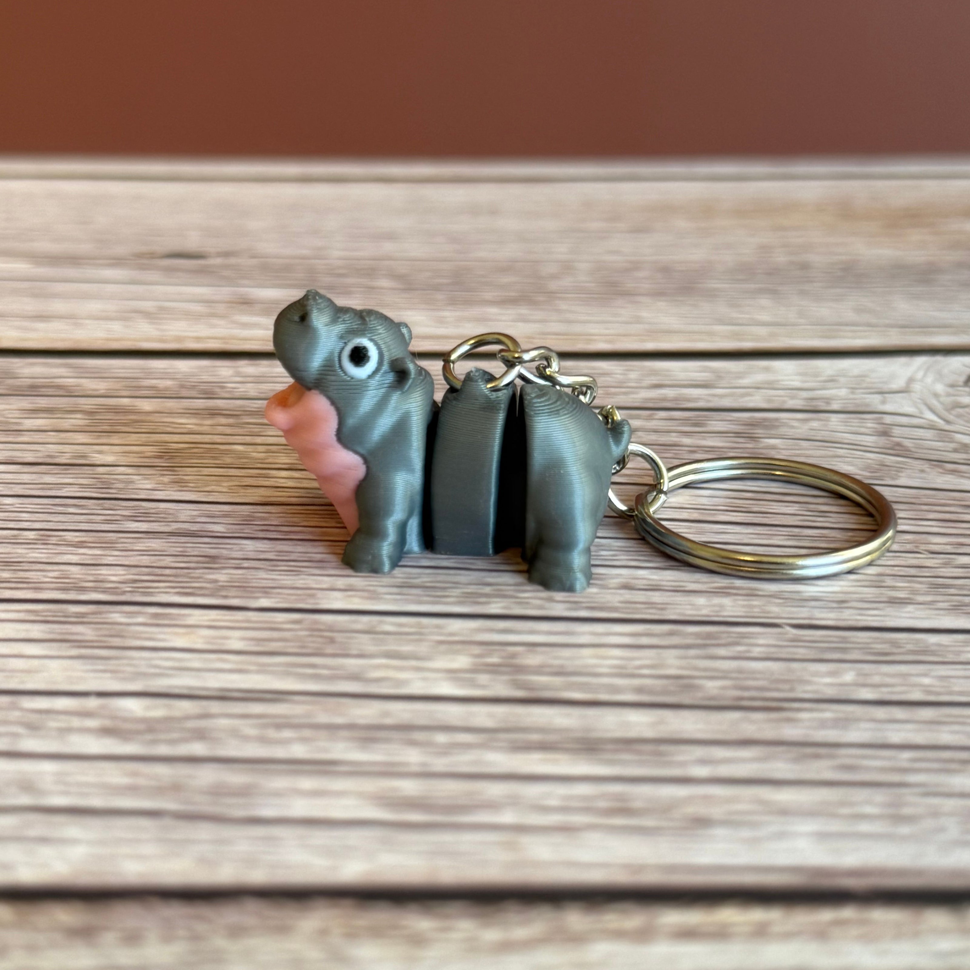 Side of a 3D printed gray and pink hippo-shaped keychain on a wooden surface