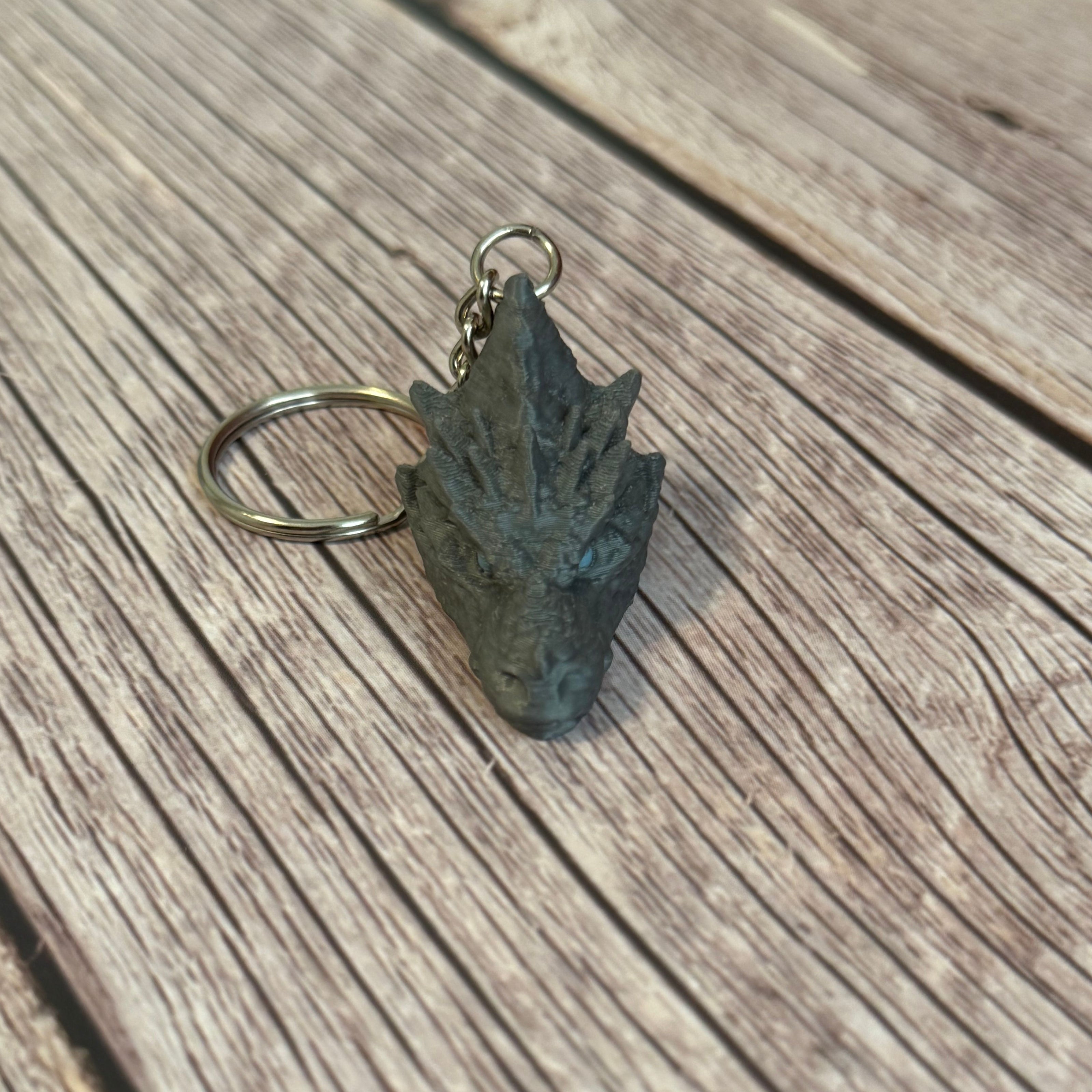 3D printed gray dragon head keychain with blue eyes on a wooden surface
