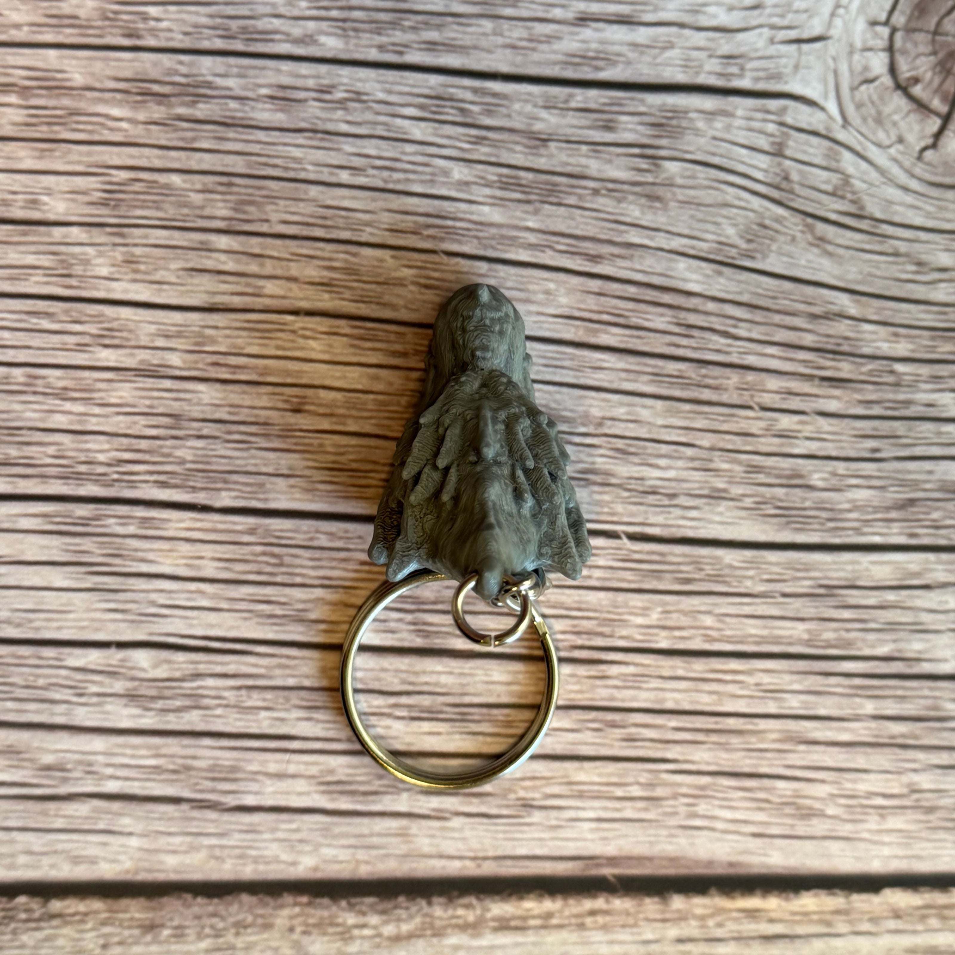 Top of a 3D printed gray dragon head keychain with blue eyes on a wooden surface