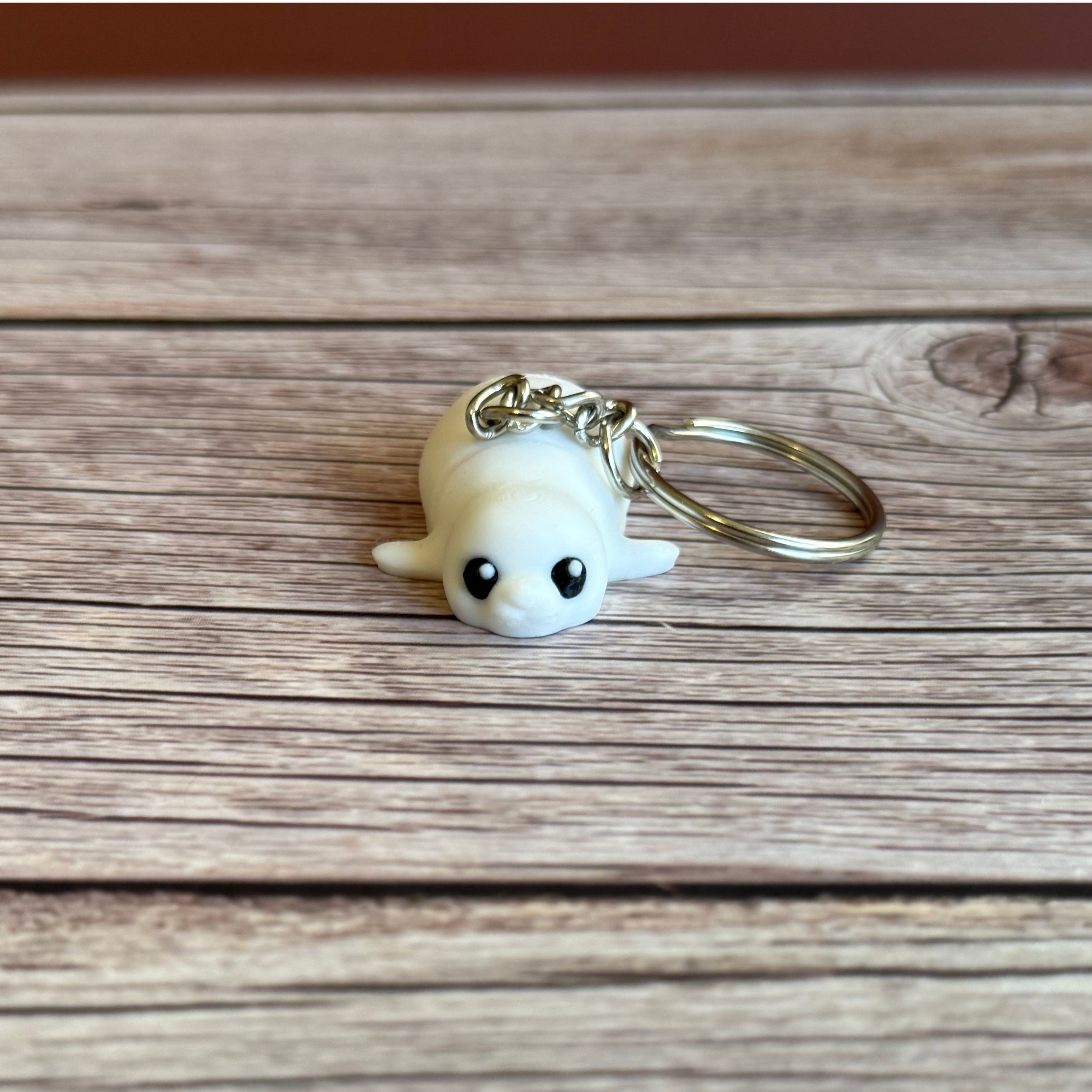 3D printed white seal-shaped keychain on a wooden surface