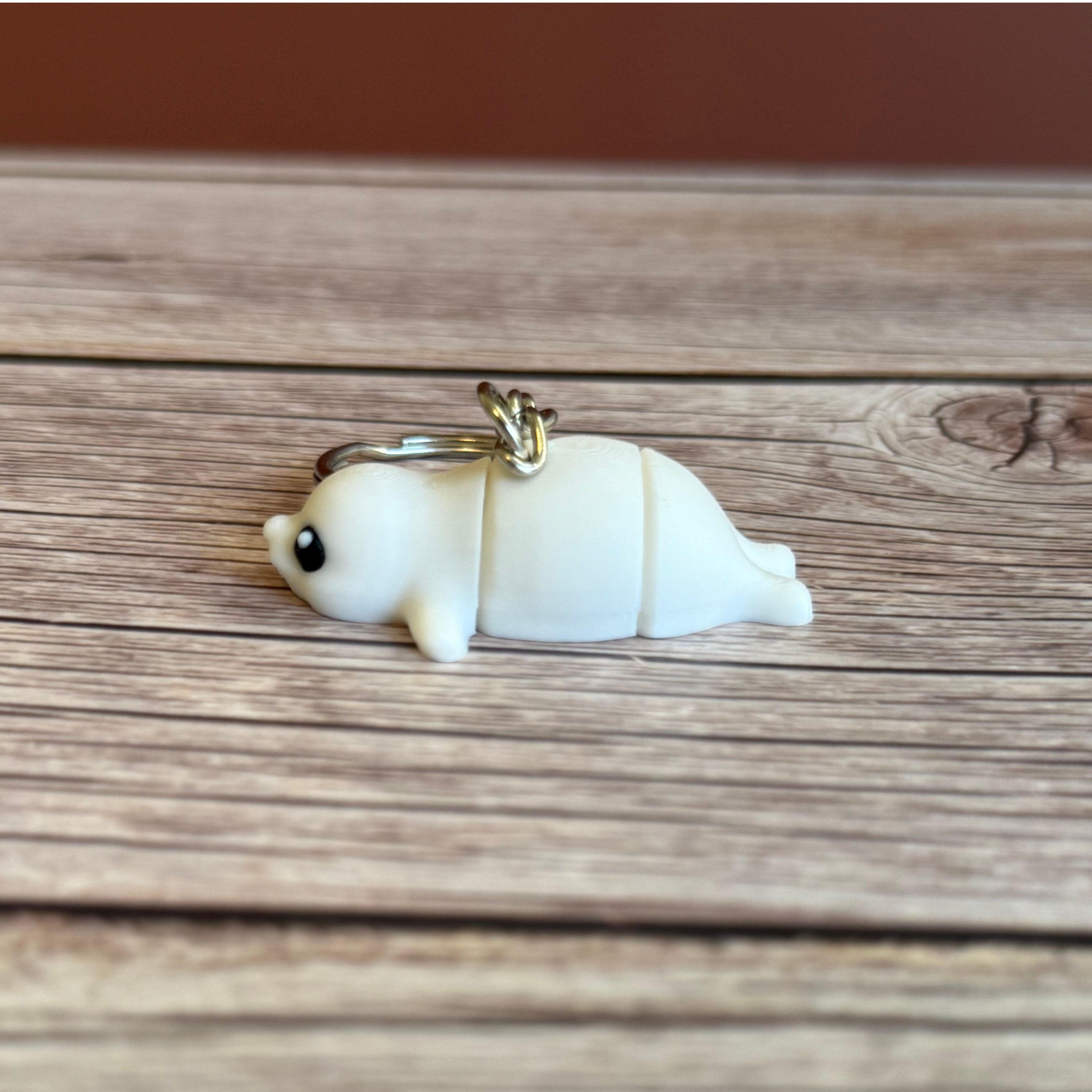 Side of a 3D printed white seal-shaped keychain on a wooden surface