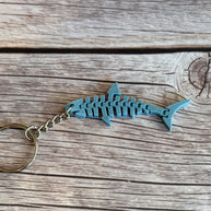 3D printed blue-gray flat flexi shark keychain on a wooden background.