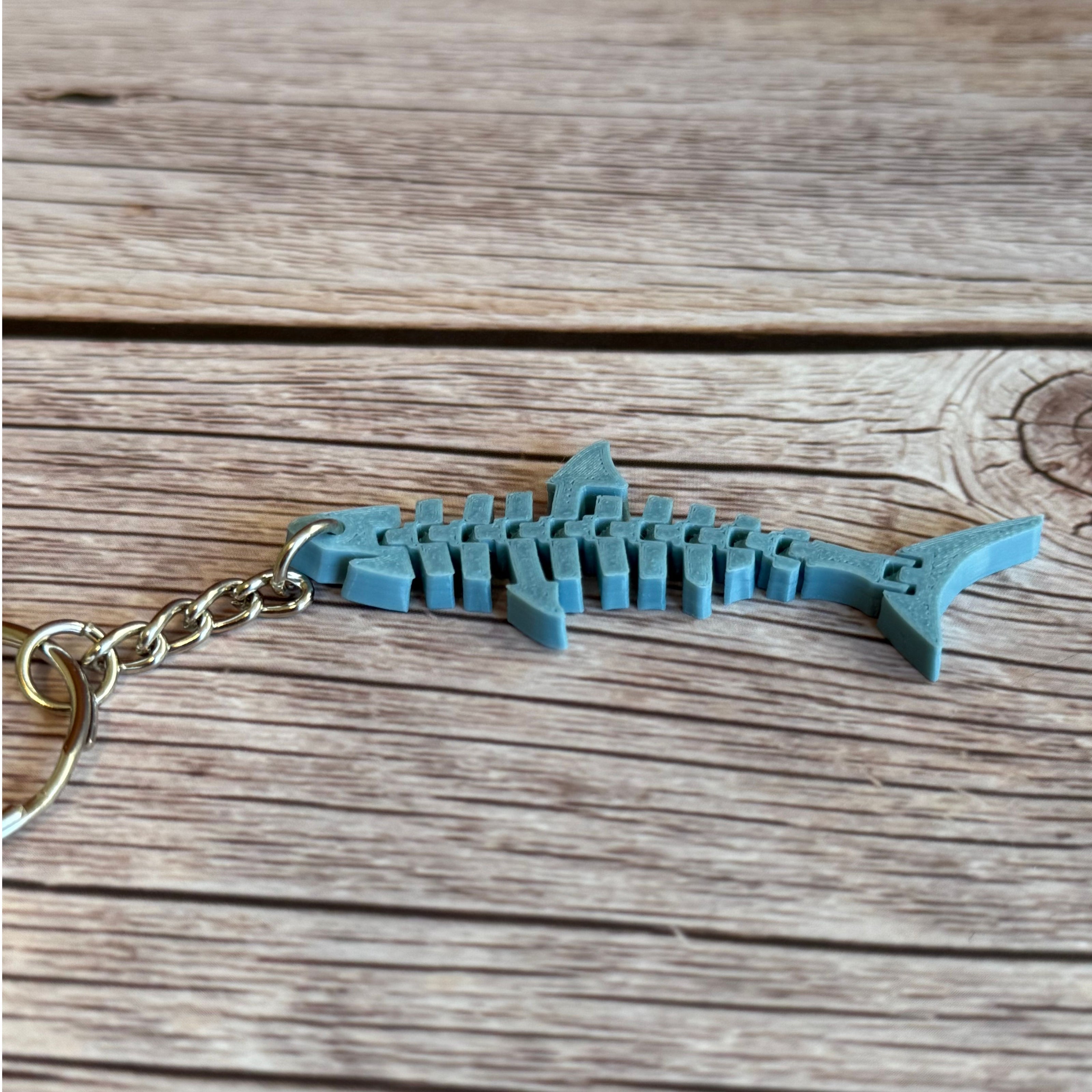 3D printed blue-gray flat flexi shark keychain on a wooden surface