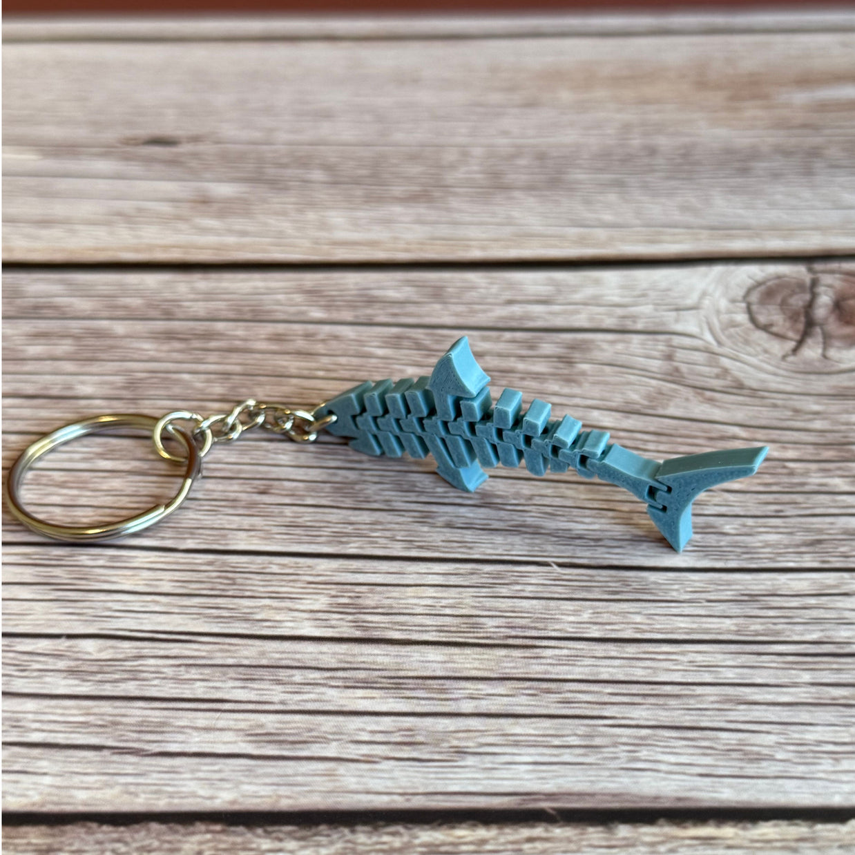 3D printed blue-gray flat flexi shark keychain on a wooden surface