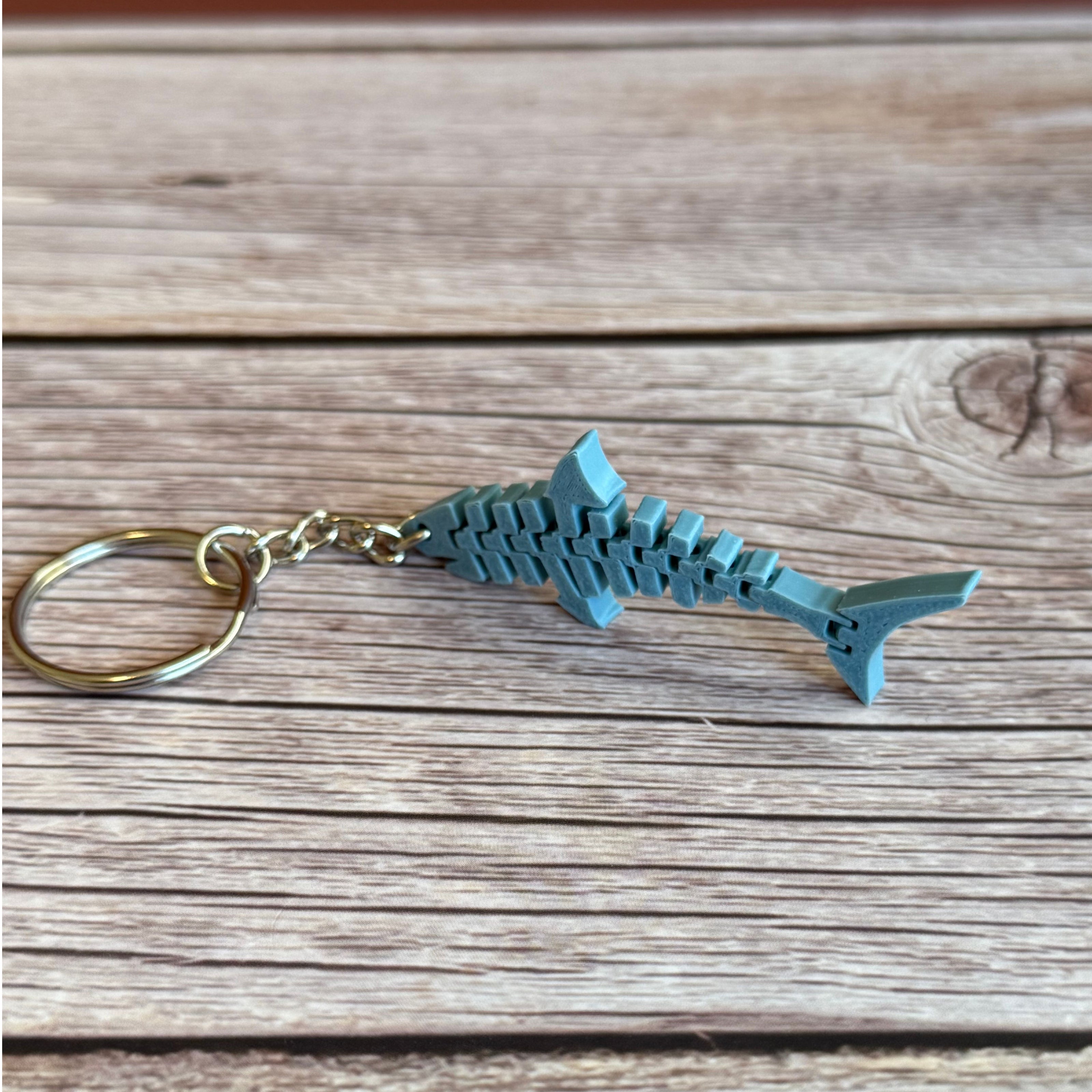3D printed blue-gray flat flexi shark keychain on a wooden surface