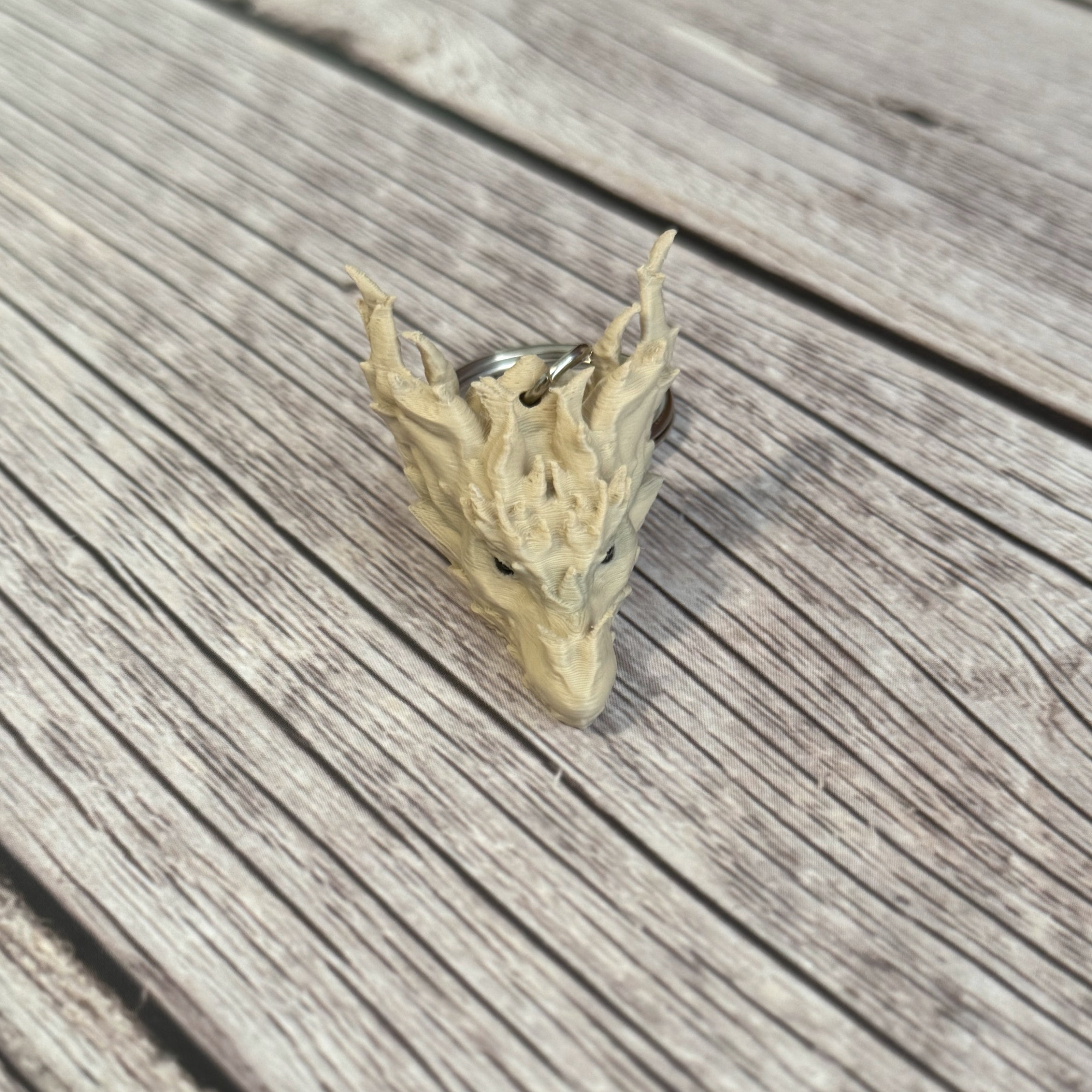 3D printed beige dragon head keychain on a wooden surface