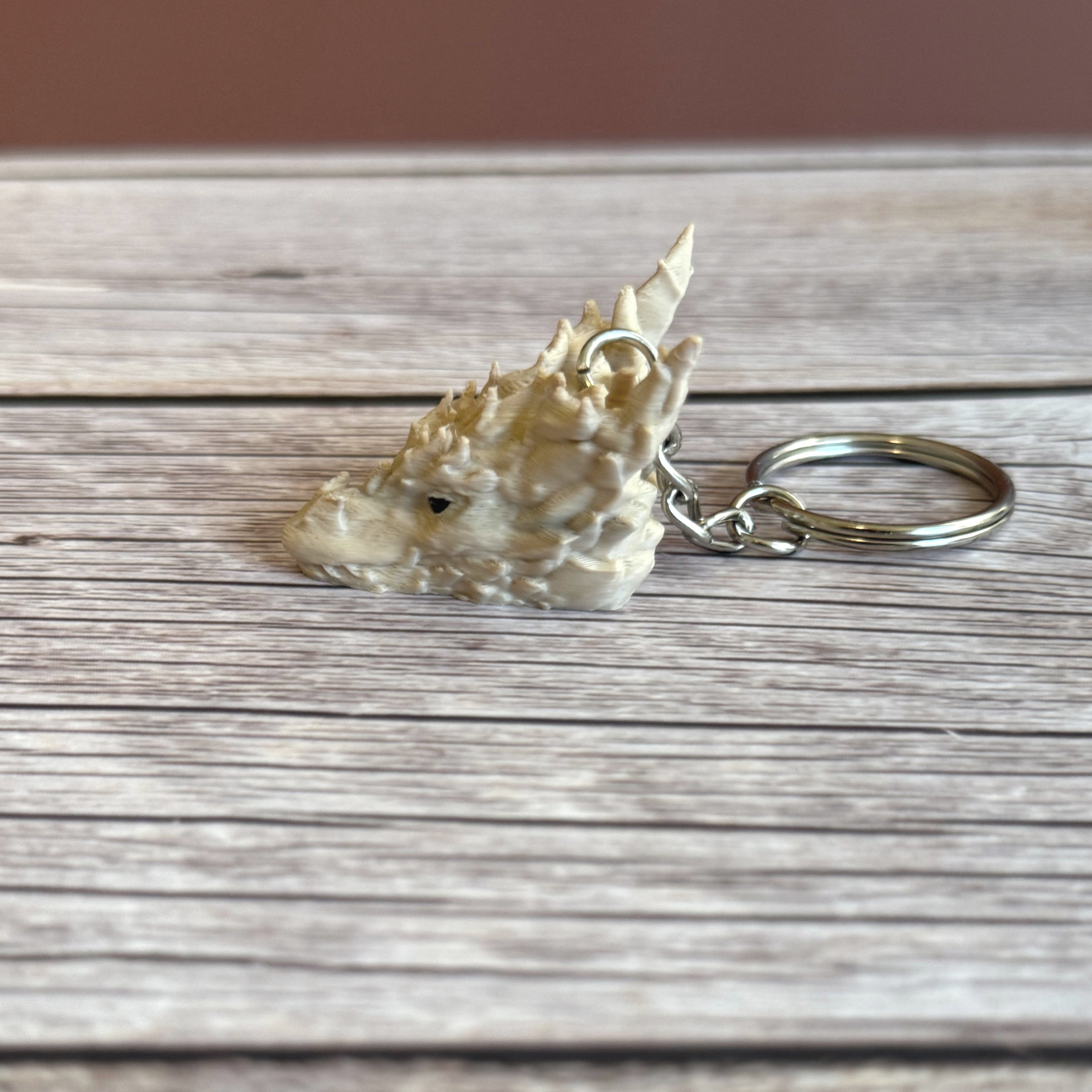 Side of a 3D printed beige dragon head keychain on a wooden surface