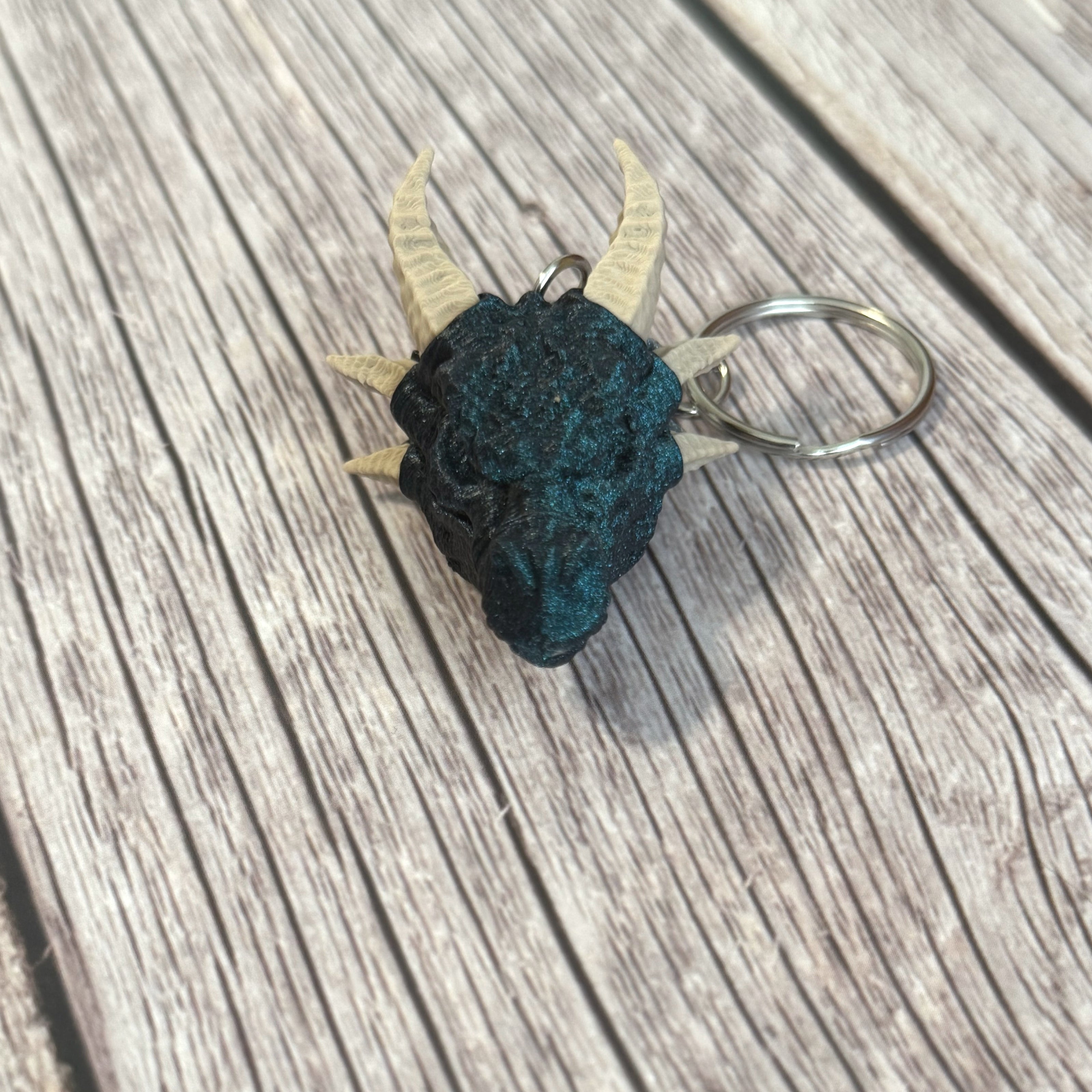3D printed blue dragon head keychain with beige horns on a wooden surface