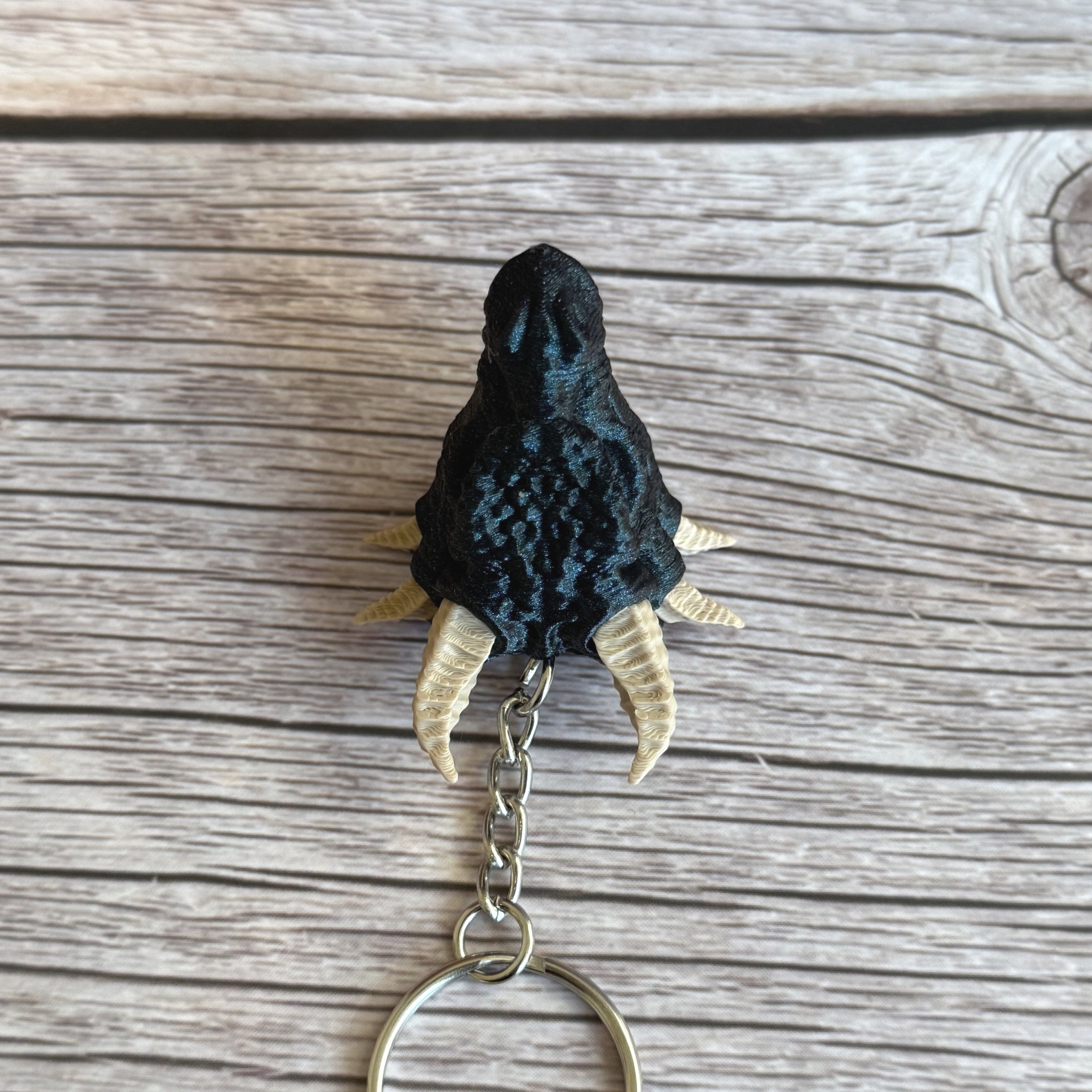 Top of a 3D printed blue dragon head keychain with beige horns on a wooden surface