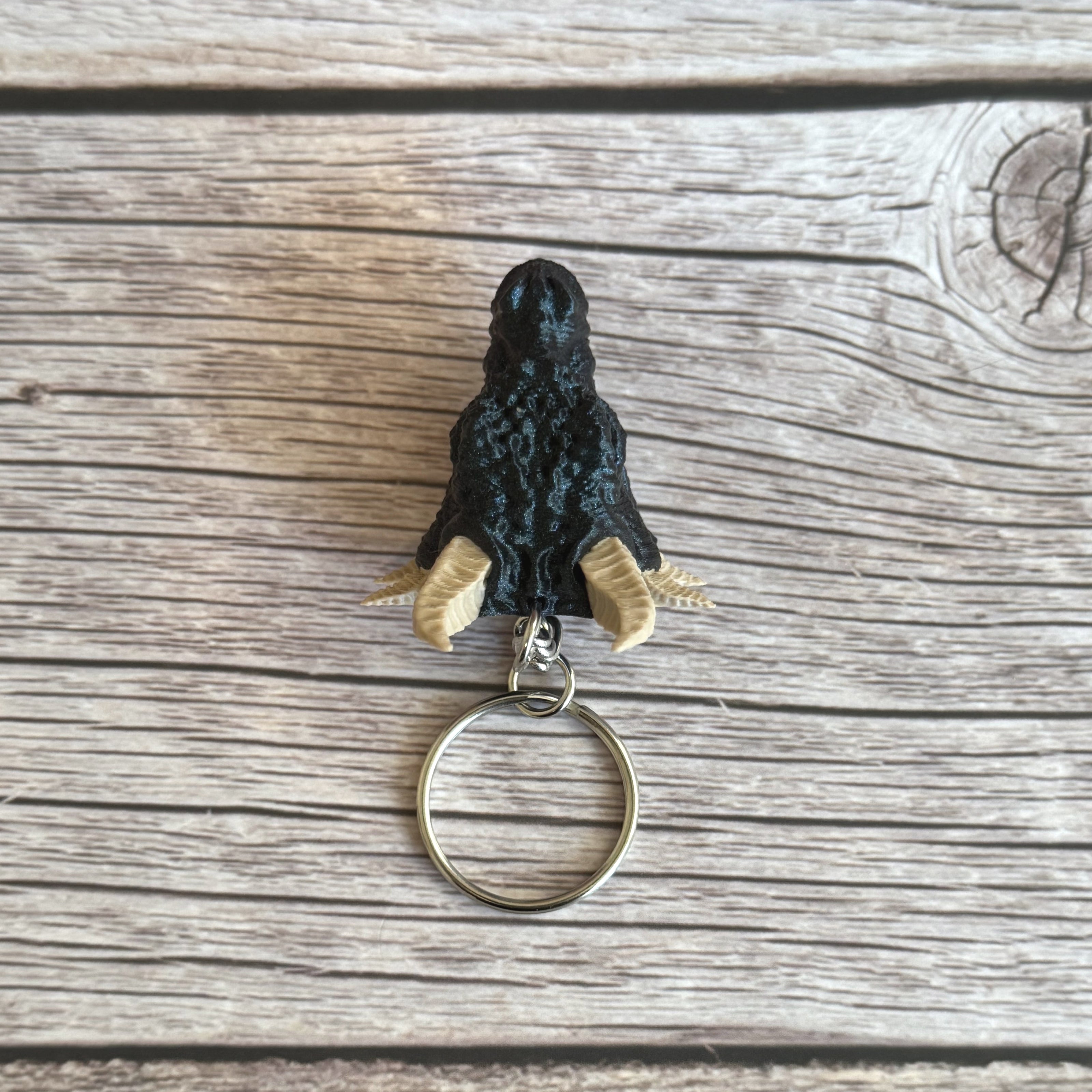Top of a 3D printed blue dragon head keychain with beige horns on a wooden surface