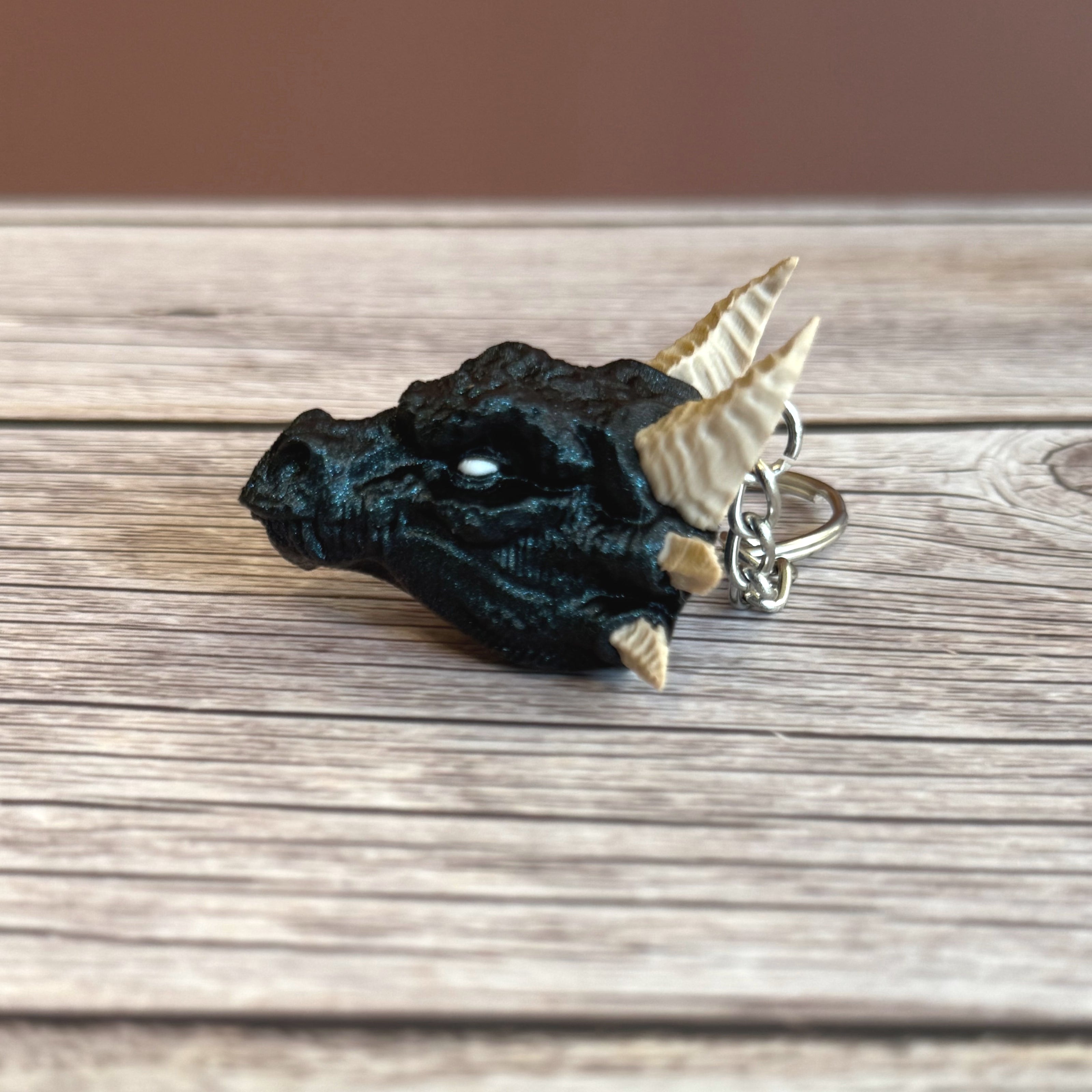 Side of a 3D printed blue dragon head keychain with beige horns on a wooden surface