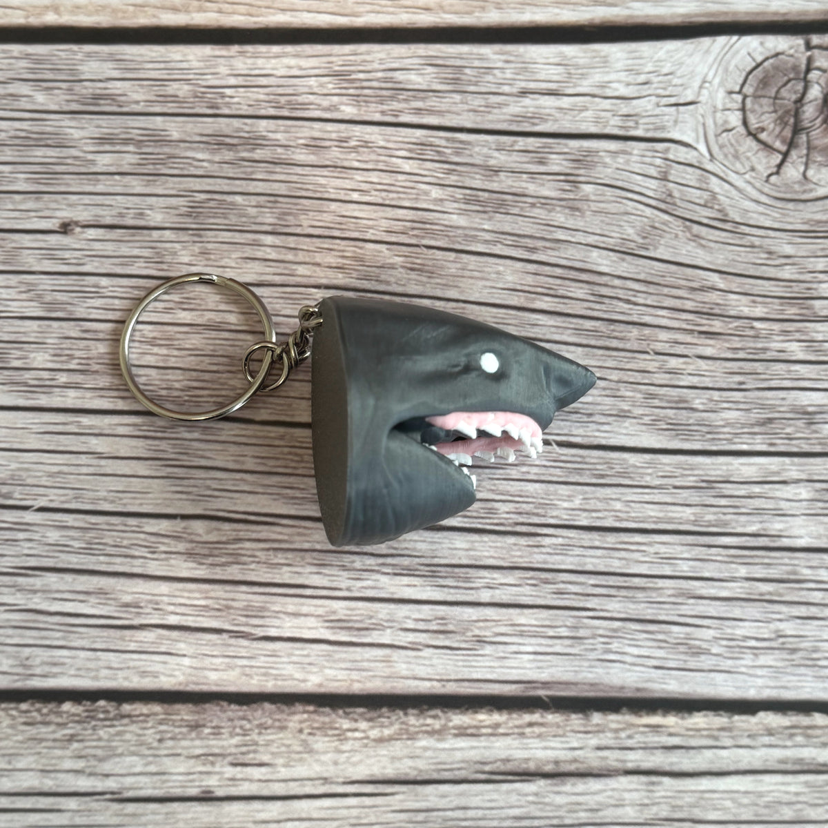 Side of a 3D printed gray keychain in the shape of a shark head with open mouth, set on a wooden surface