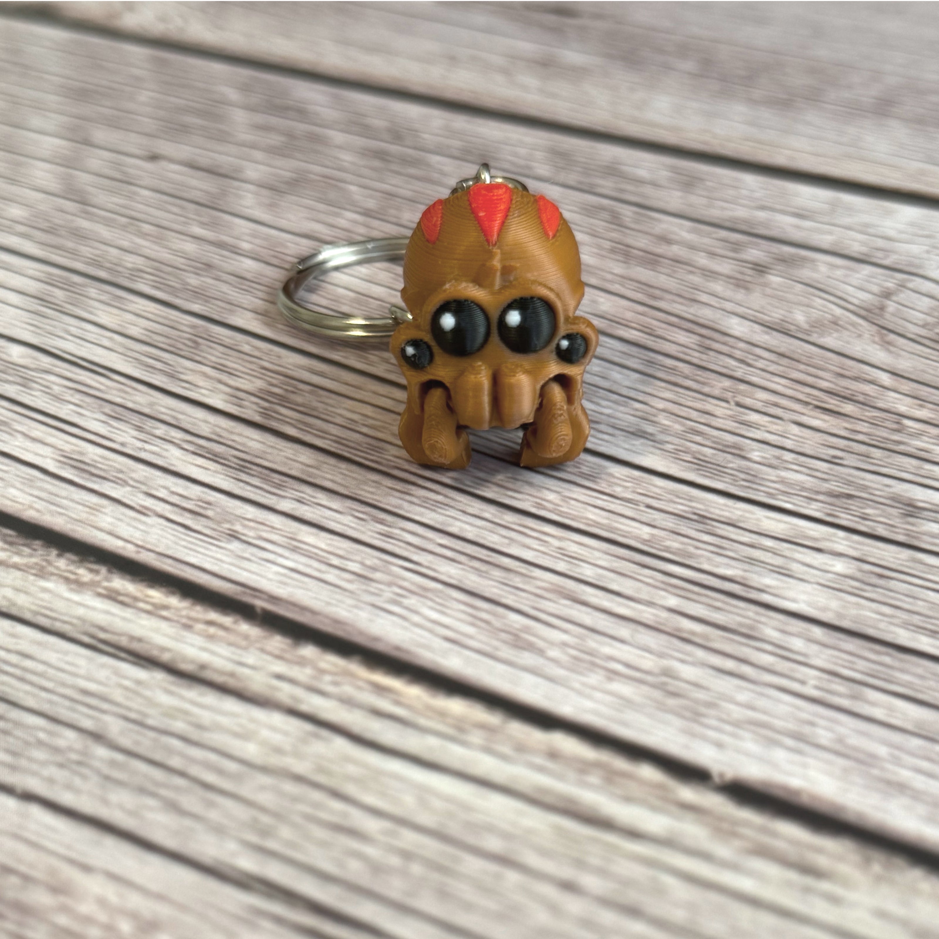 3D printed brown and red tarantula-shaped keychain with legs curled under, placed on a wooden surface