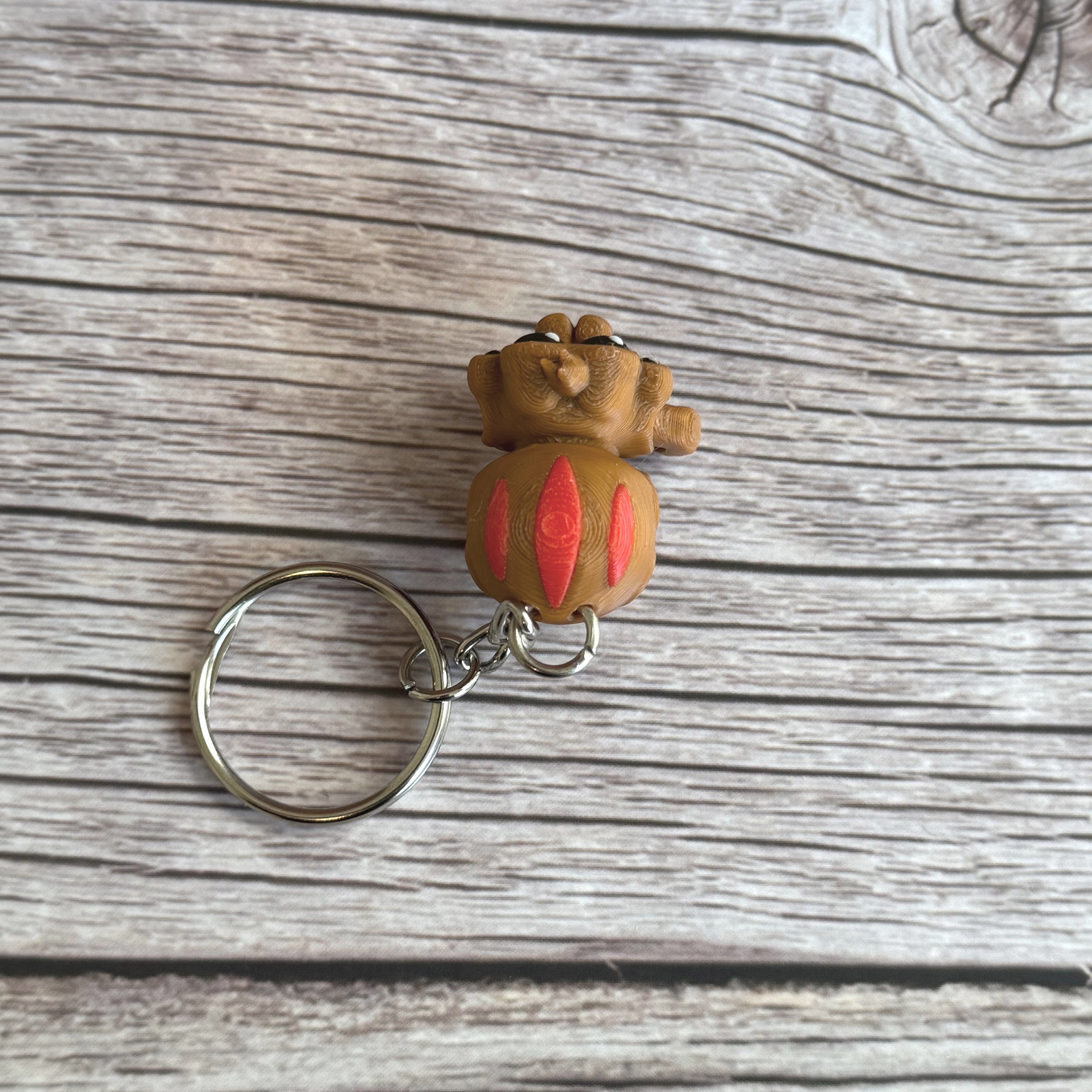 Top of a 3D printed brown and red tarantula-shaped keychain with legs curled under, placed on a wooden surface