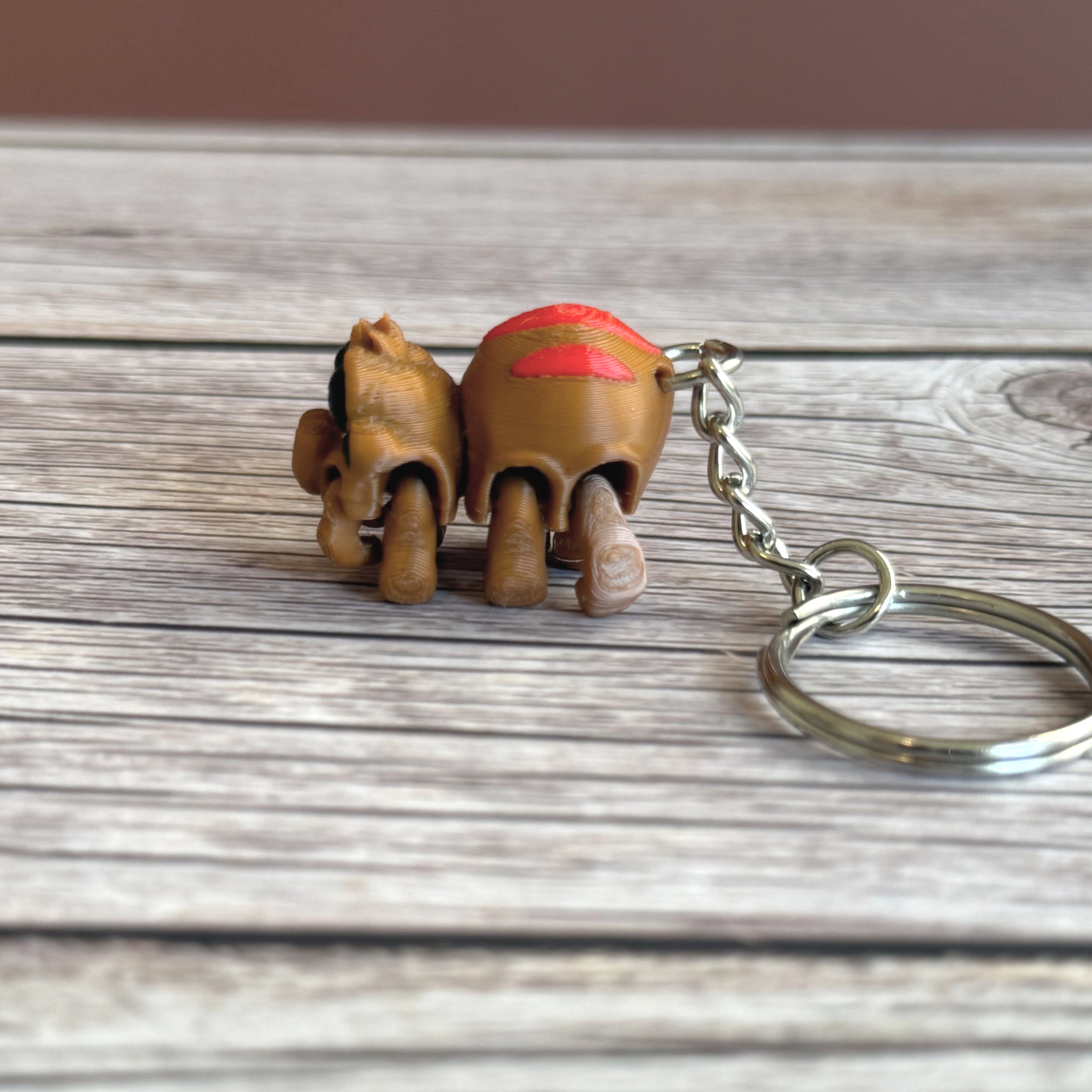 Side of a 3D printed brown and red tarantula-shaped keychain with legs curled under, placed on a wooden surface
