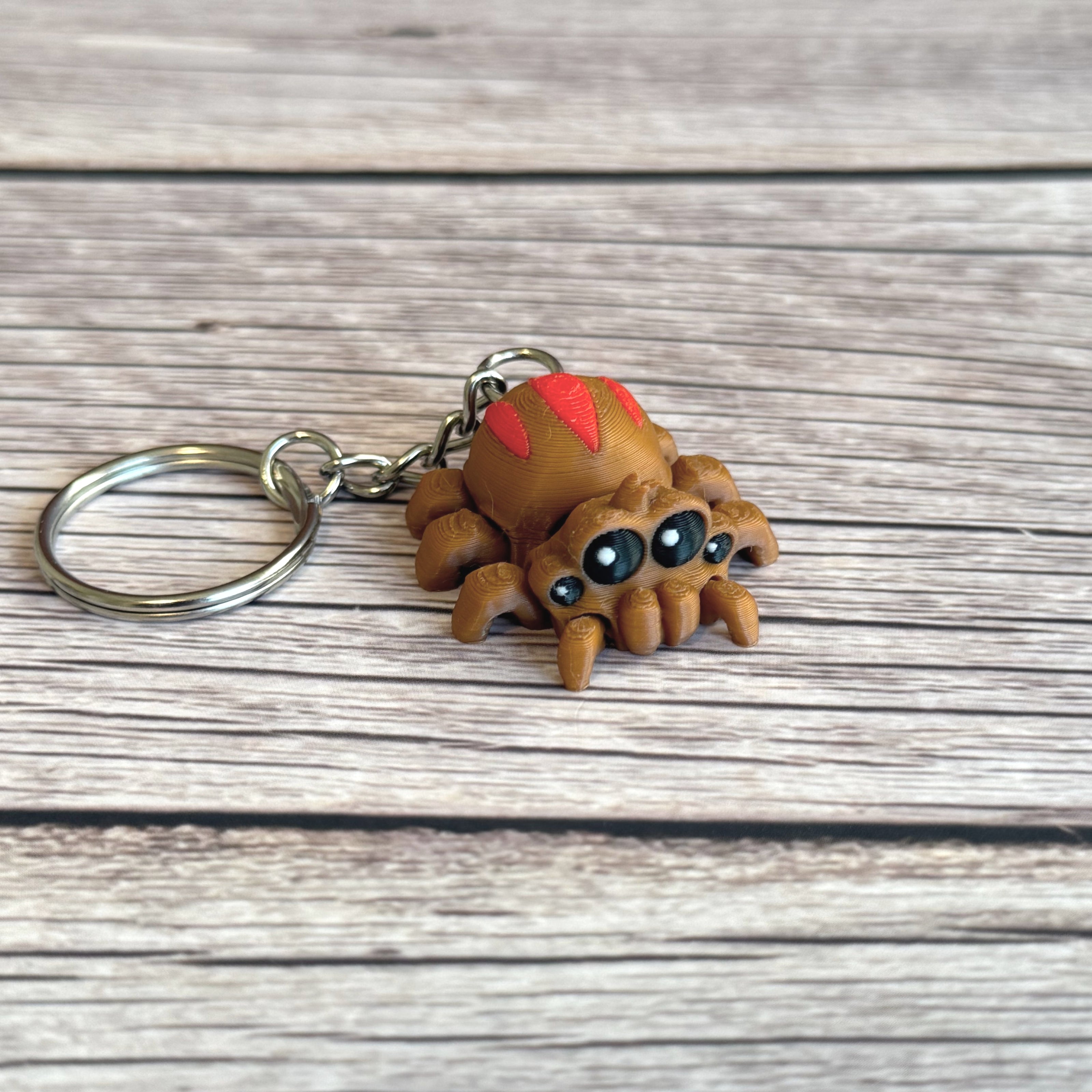 3D printed brown and red tarantula-shaped keychain with legs flat out on a wooden surface