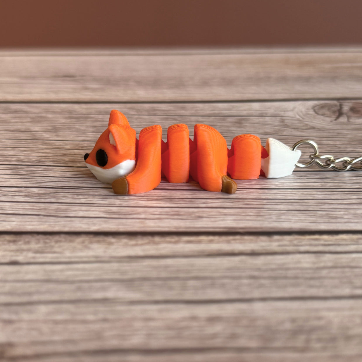 Side of a 3D printed orange fox-shaped keychain on a wooden surface