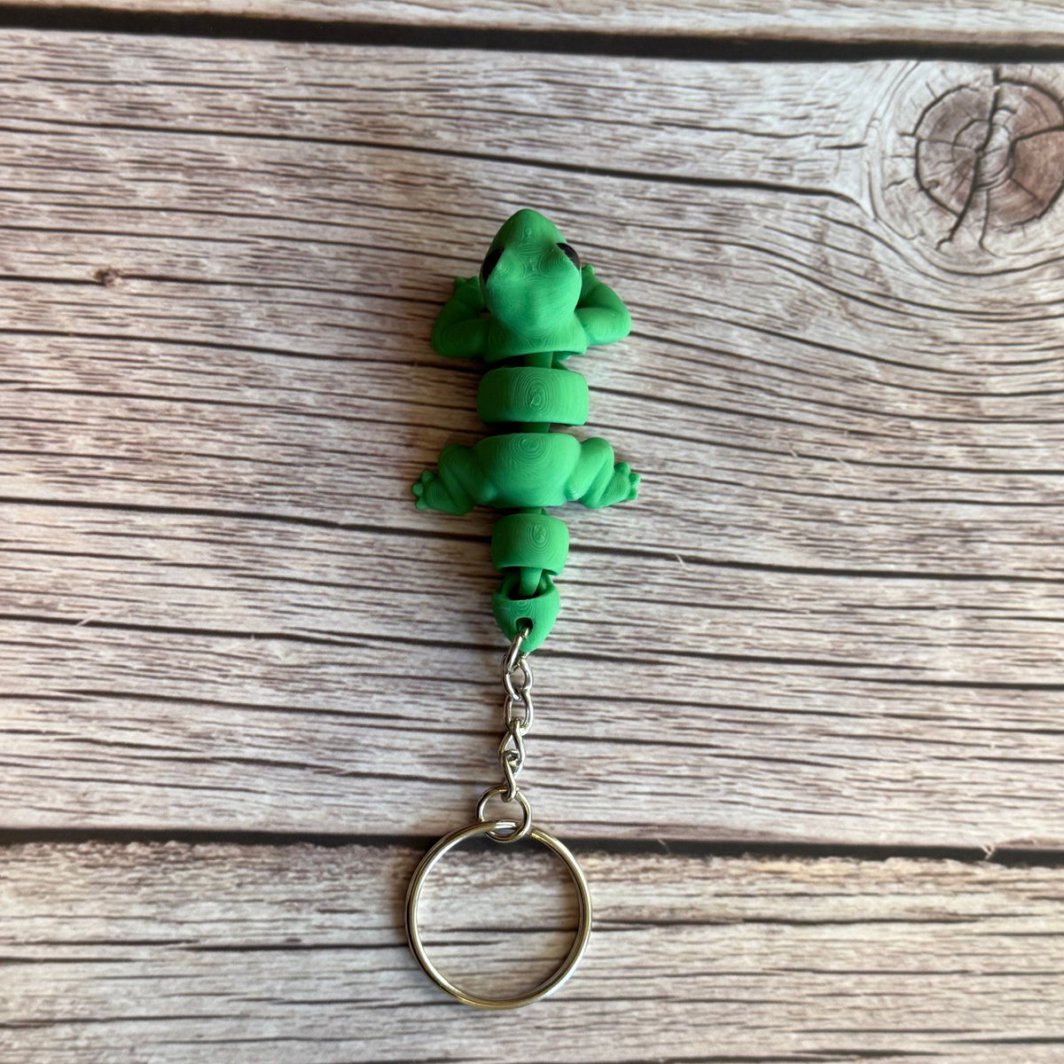 Top of a 3D printed green lizard-shaped keychain on a wooden surface
