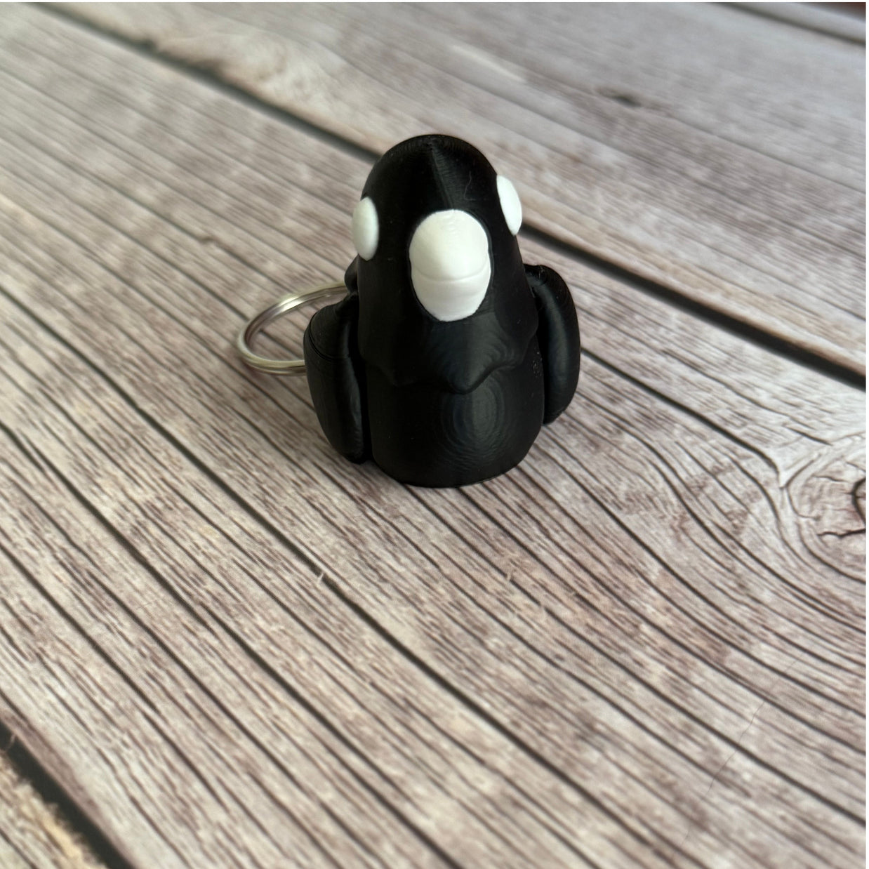 3D printed black and white crow-shaped keychain on a wooden surface