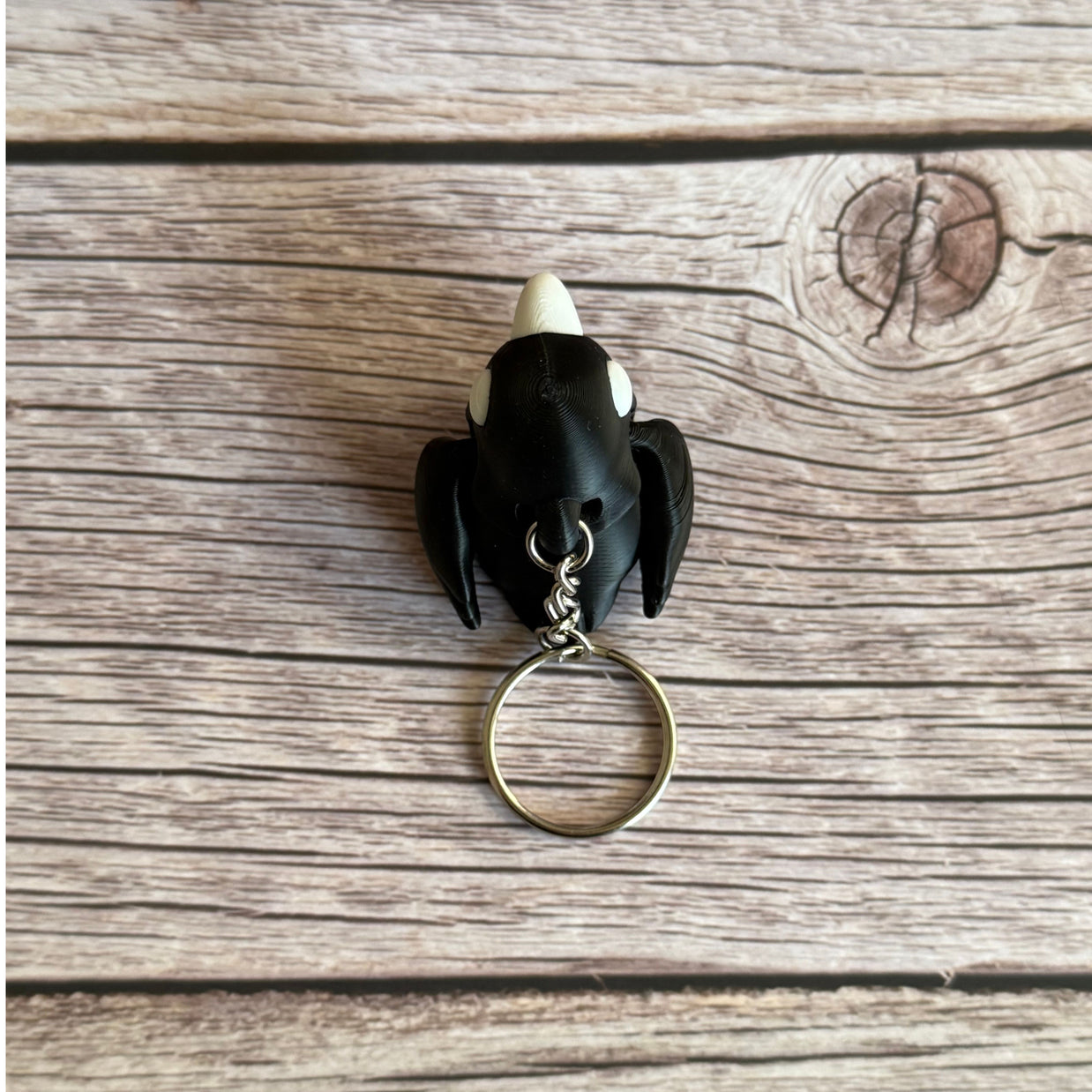 Top of a 3D printed black and white crow-shaped keychain on a wooden surface