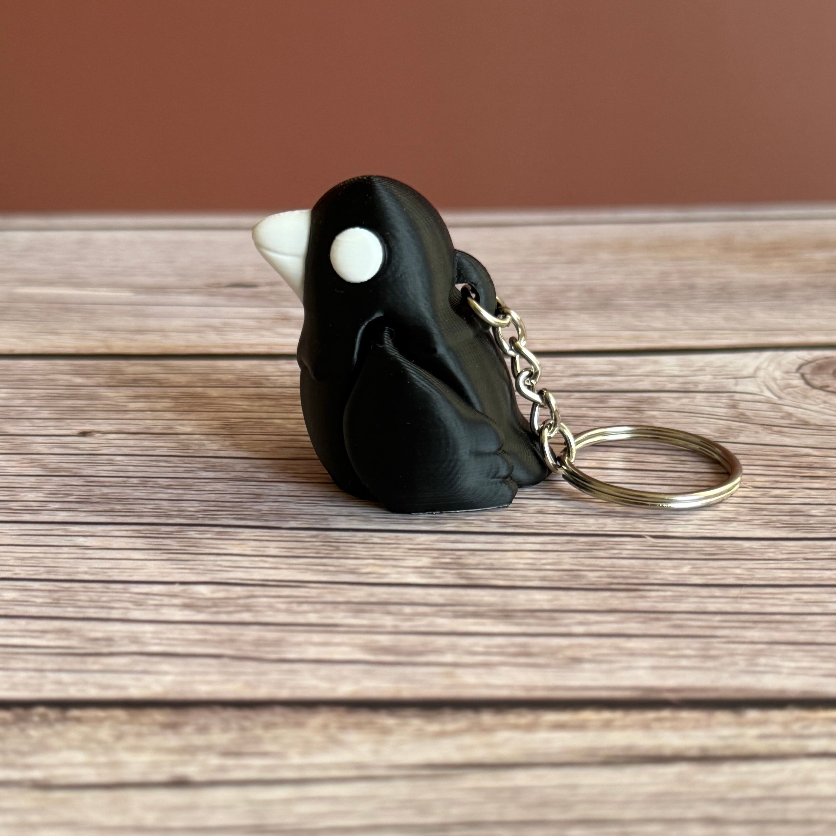 Side of a 3D printed black and white crow-shaped keychain on a wooden surface