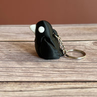 Side of a 3D printed black and white crow-shaped keychain on a wooden surface