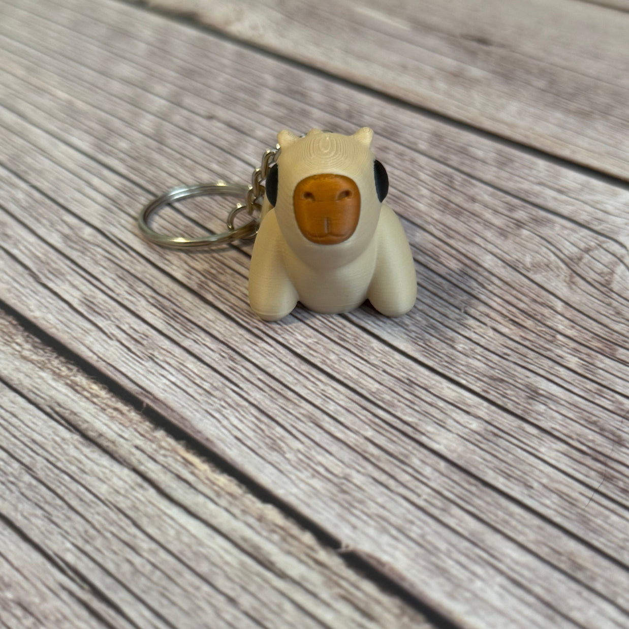 3D printed beige capybara-shaped keychain on a wooden surface