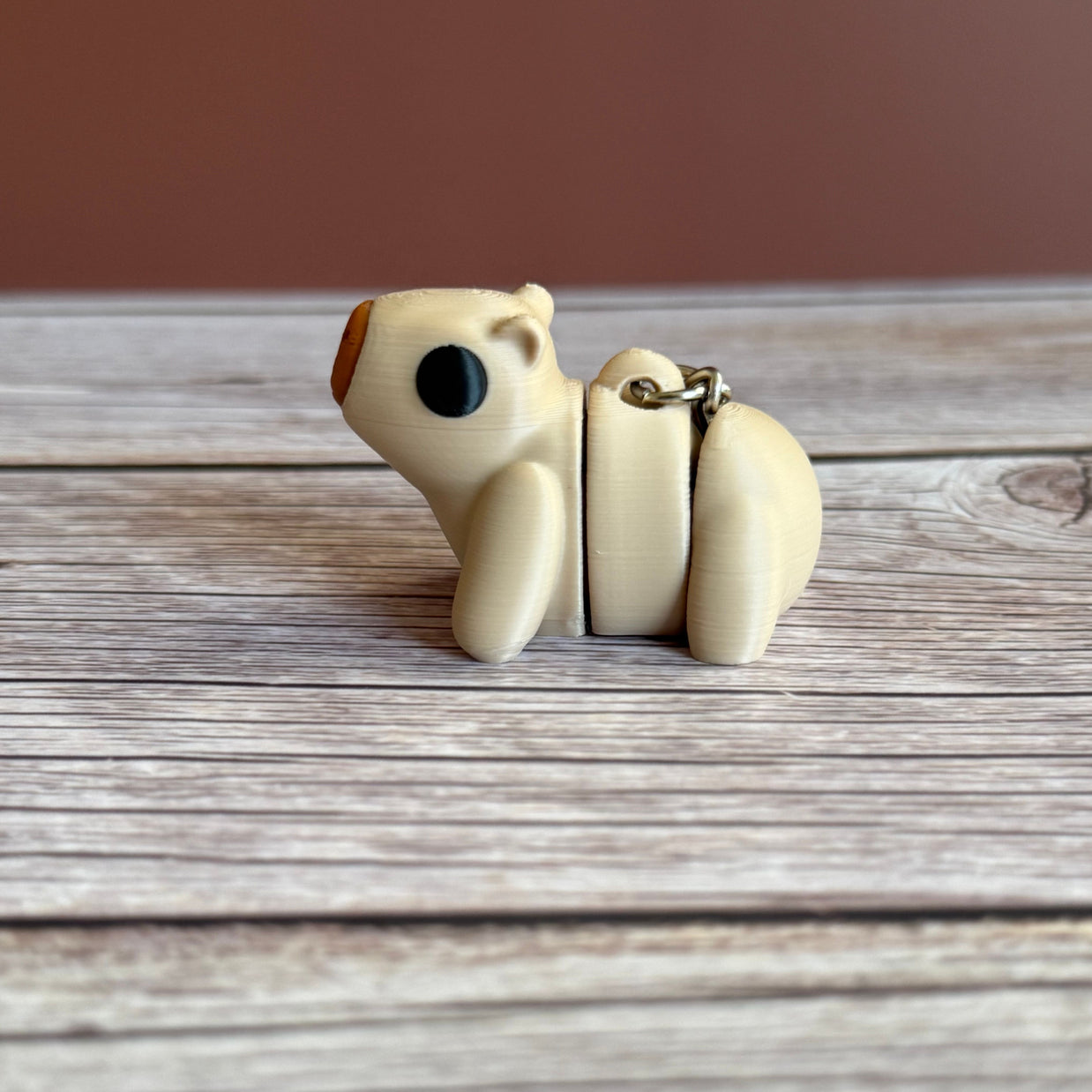 Side of a 3D printed beige capybara-shaped keychain on a wooden surface