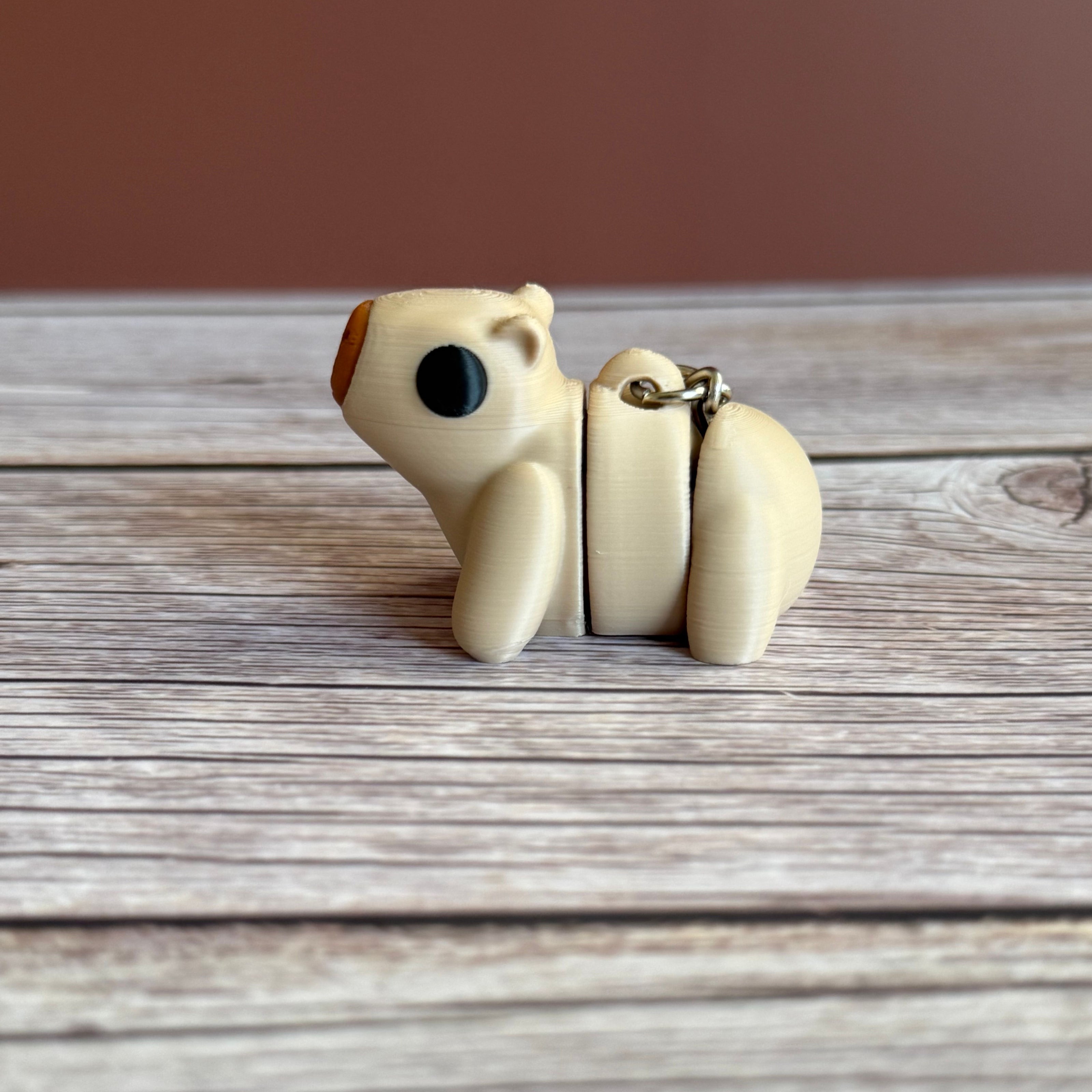 Side of a 3D printed beige capybara-shaped keychain on a wooden surface