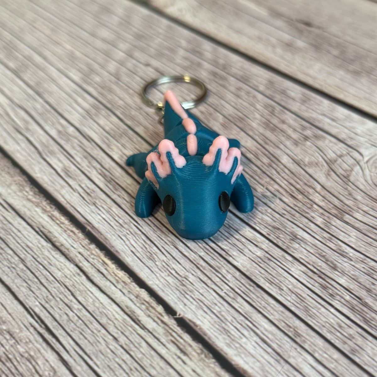 3D printed blue and pink axolotl-shaped keychain on a wooden surface