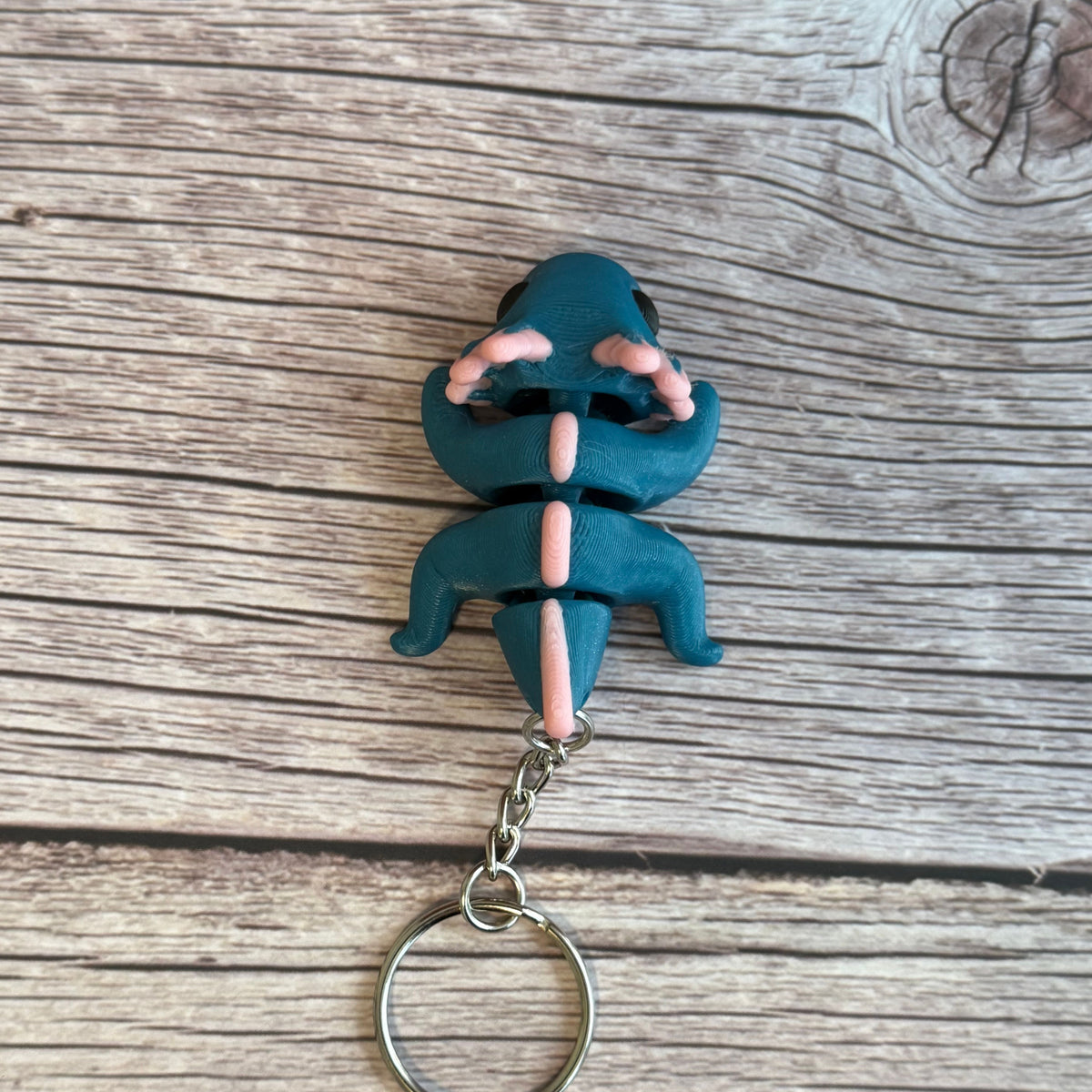 Top of a 3D printed blue and pink axolotl-shaped keychain on a wooden surface