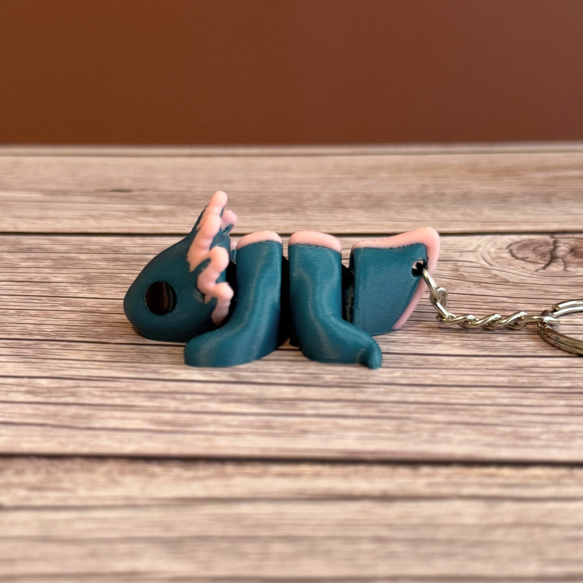 Side of a 3D printed blue and pink axolotl-shaped keychain on a wooden surface