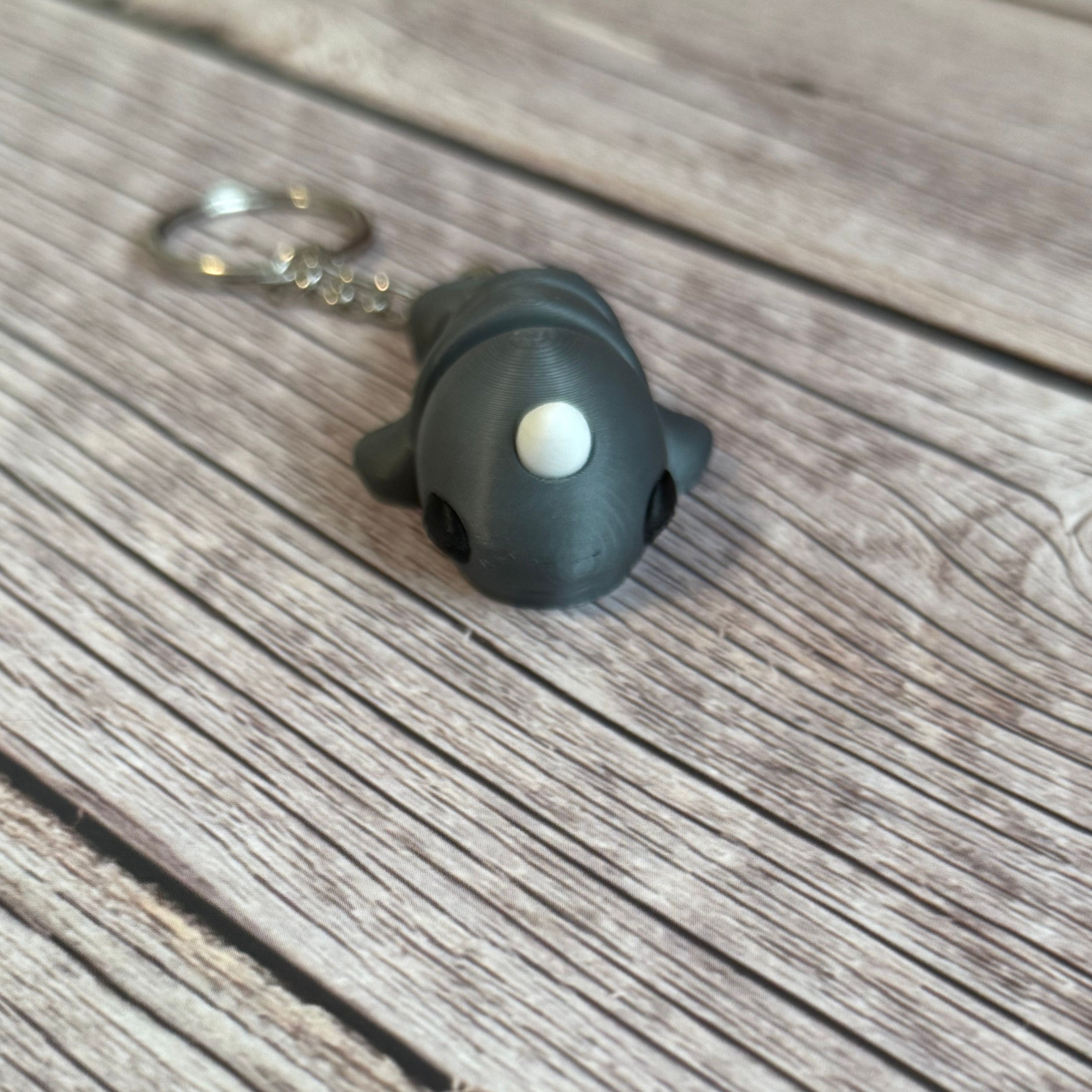 3D printed gray narwhal-shaped keychain on a wooden surface