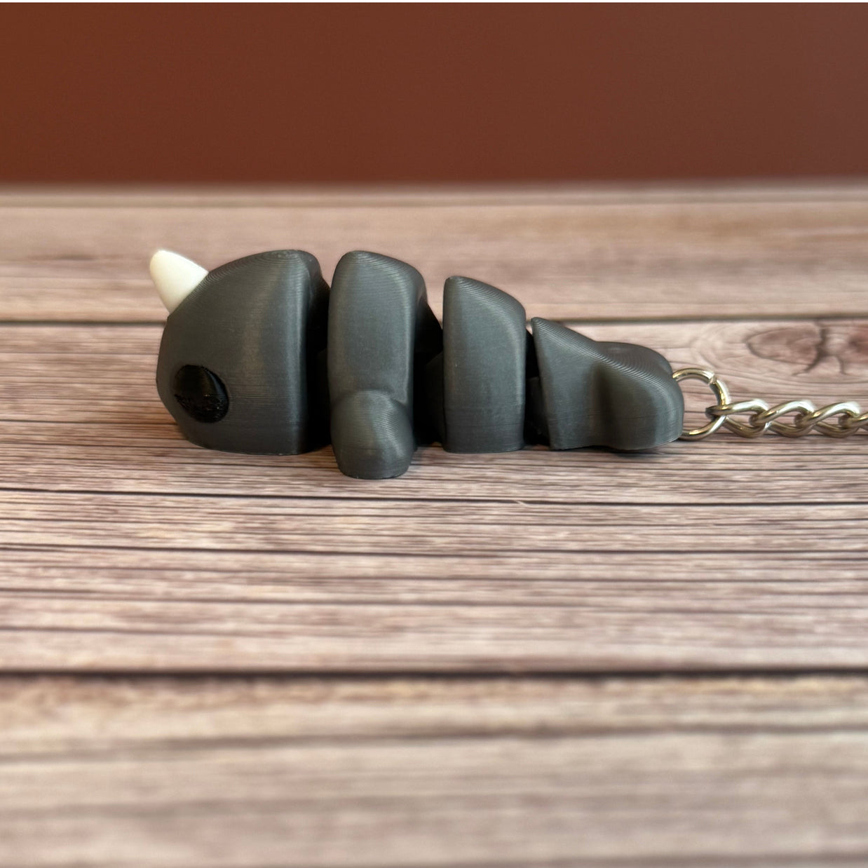 Side of a 3D printed gray narwhal-shaped keychain on a wooden surface