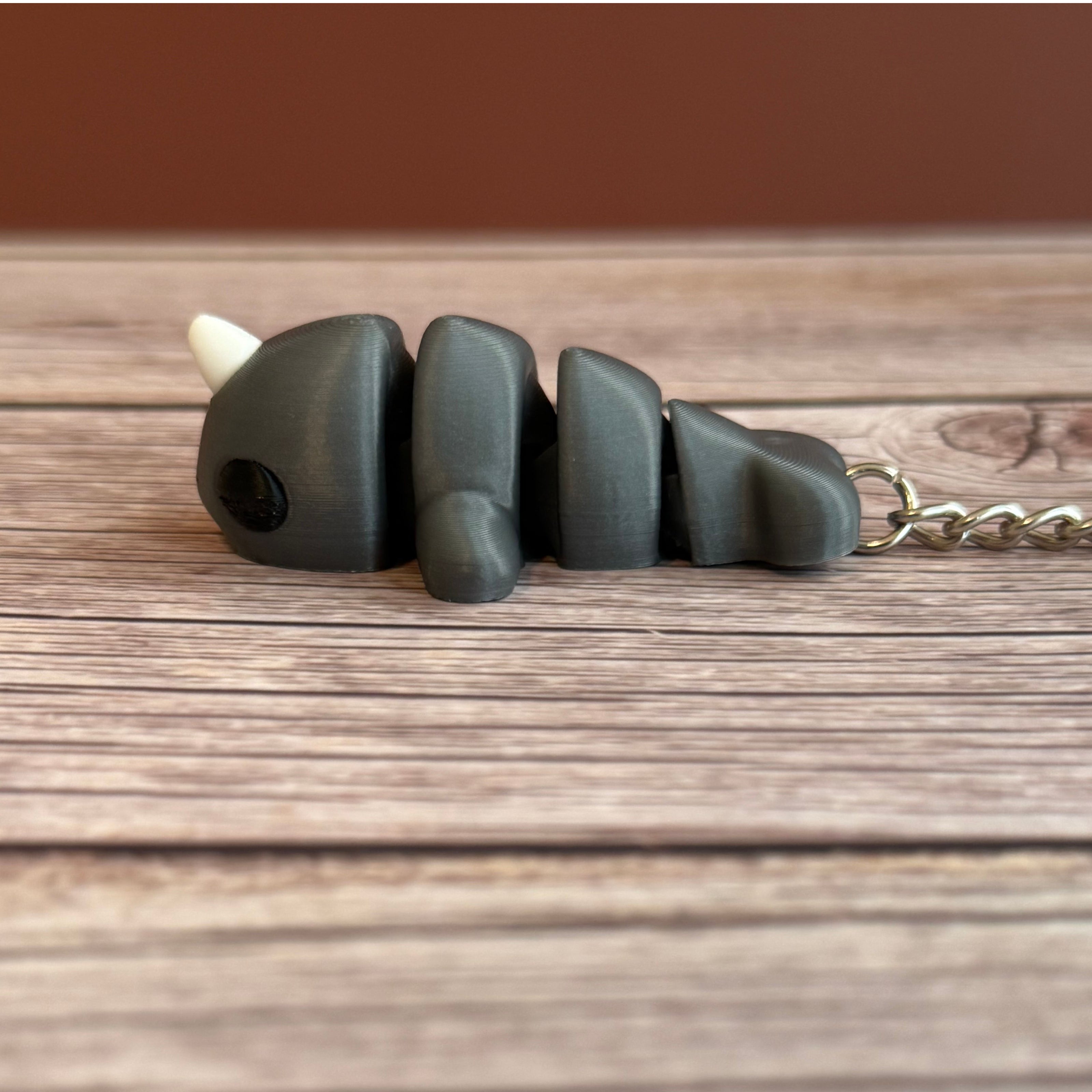 Side of a 3D printed gray narwhal-shaped keychain on a wooden surface