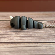 Side of a 3D printed gray narwhal-shaped keychain on a wooden surface