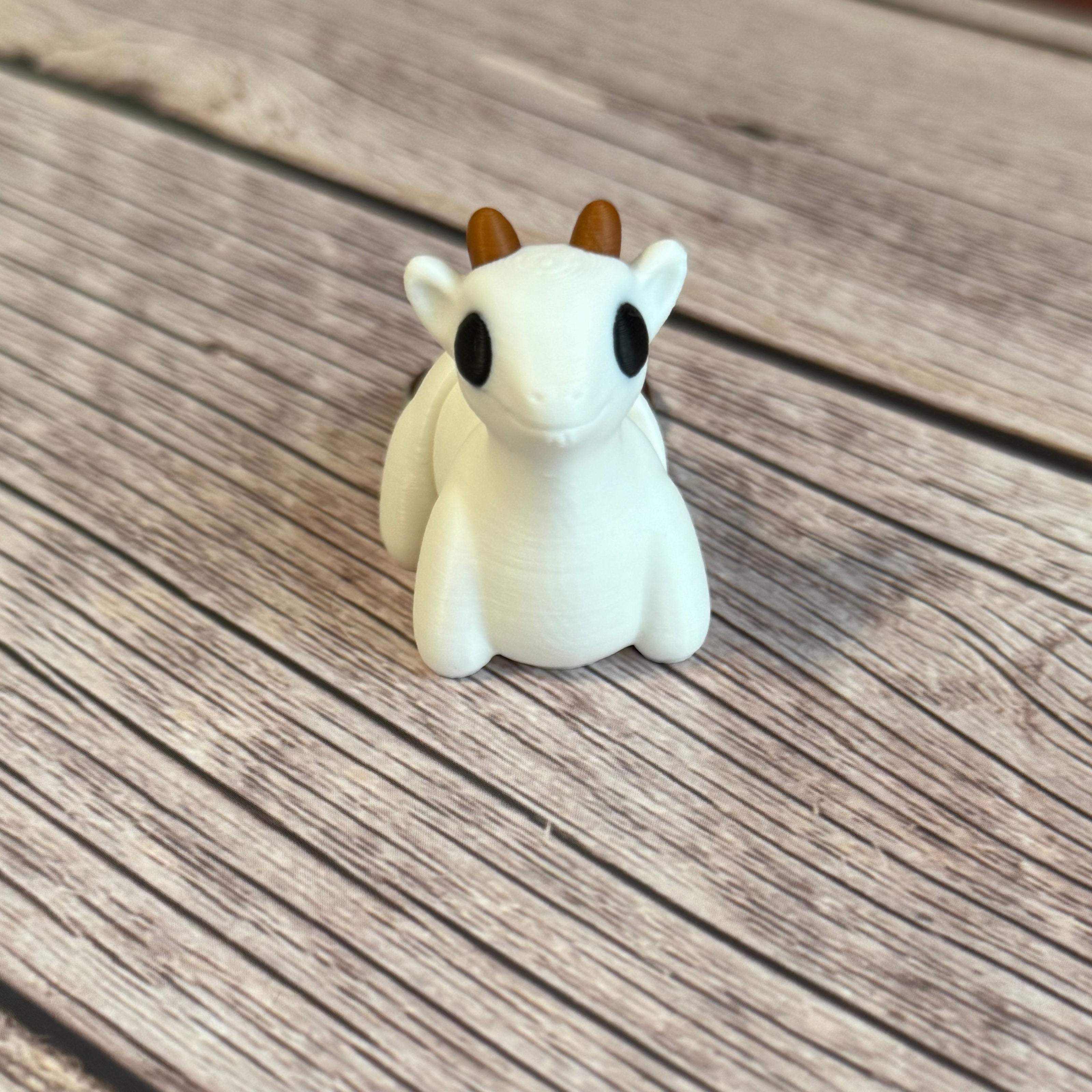 3D printed white goat-shaped keychain with brown horns on a wooden surface