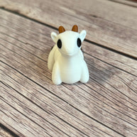 3D printed white goat-shaped keychain with brown horns on a wooden surface