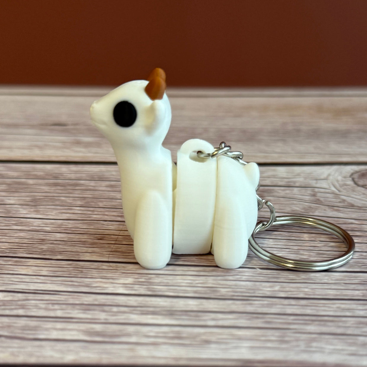 Side of a 3D printed white goat-shaped keychain with brown horns on a wooden surface