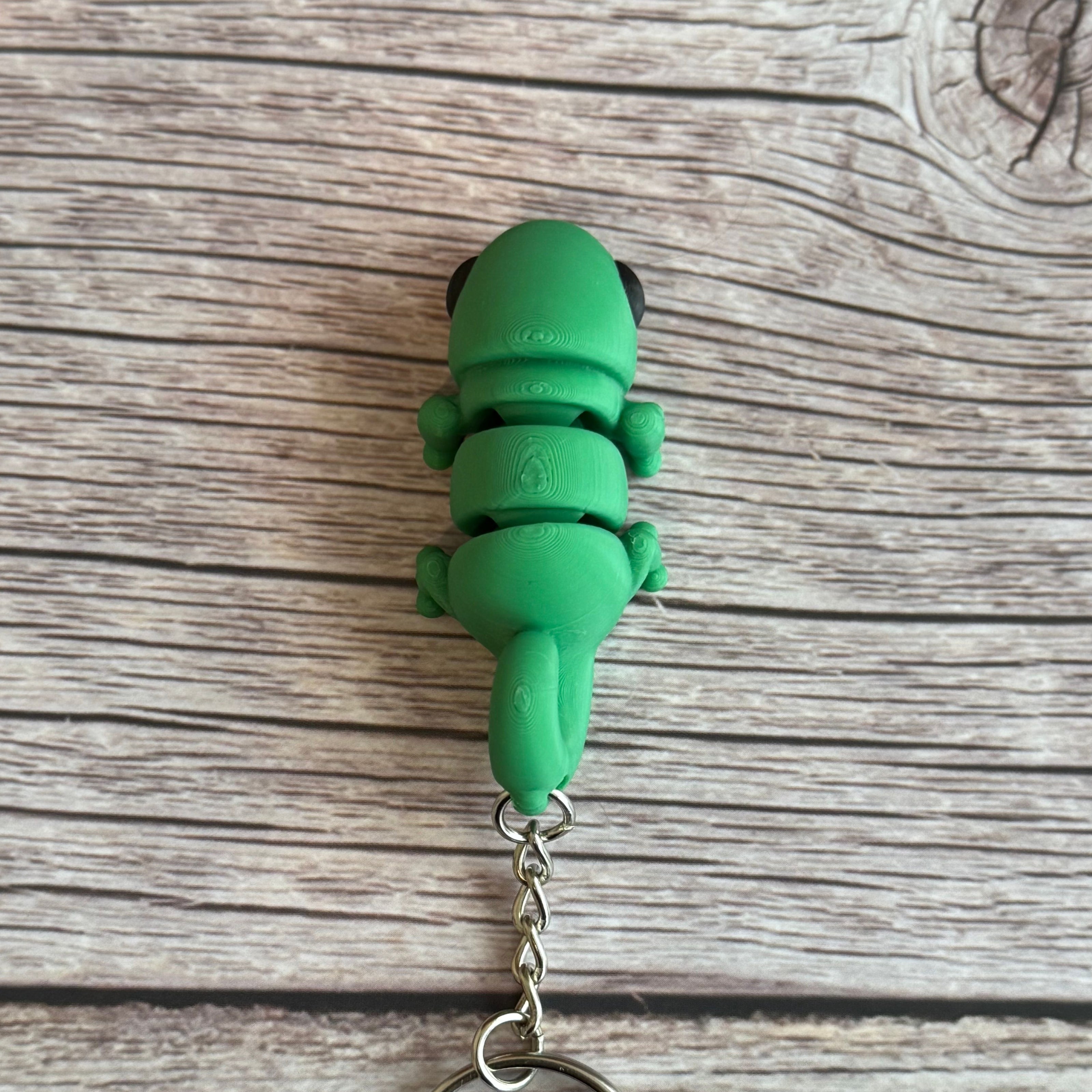 Top of a 3D printed green chameleon-shaped keychain on a wooden surface