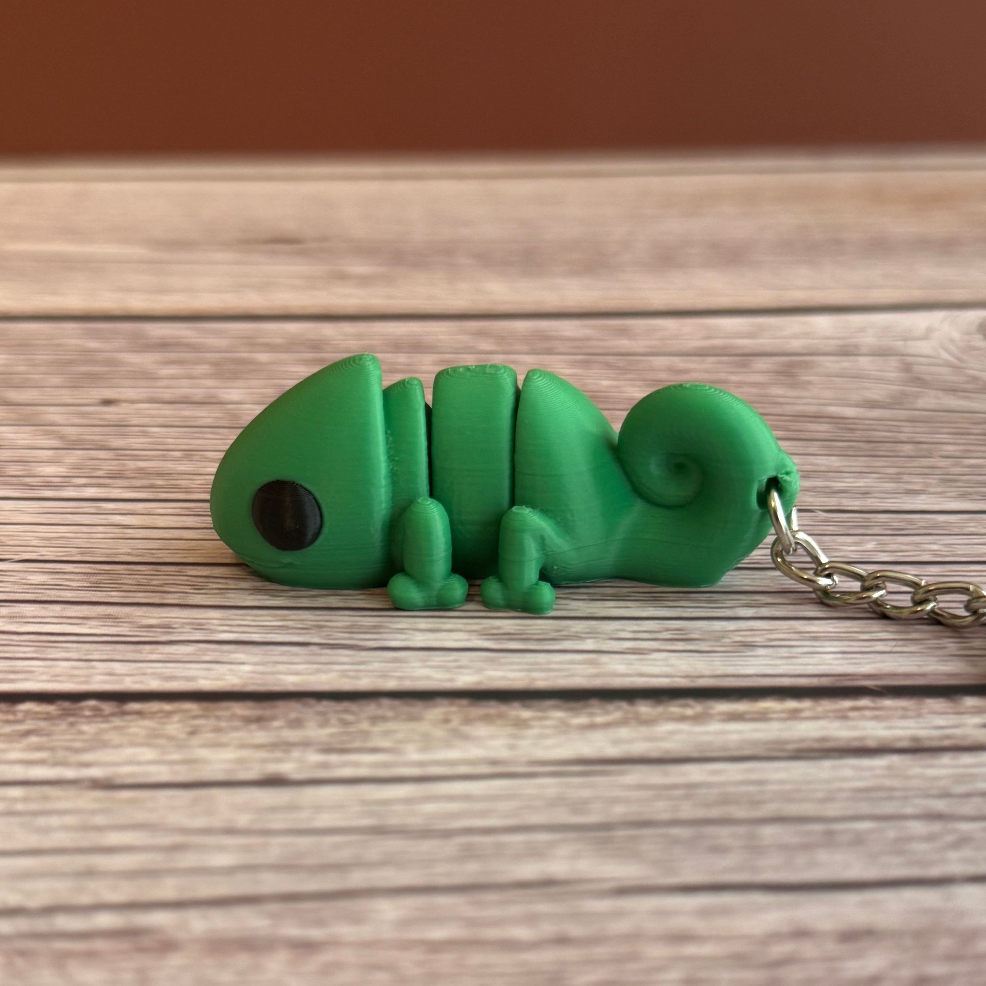 Side of a 3D printed green chameleon-shaped keychain on a wooden surface