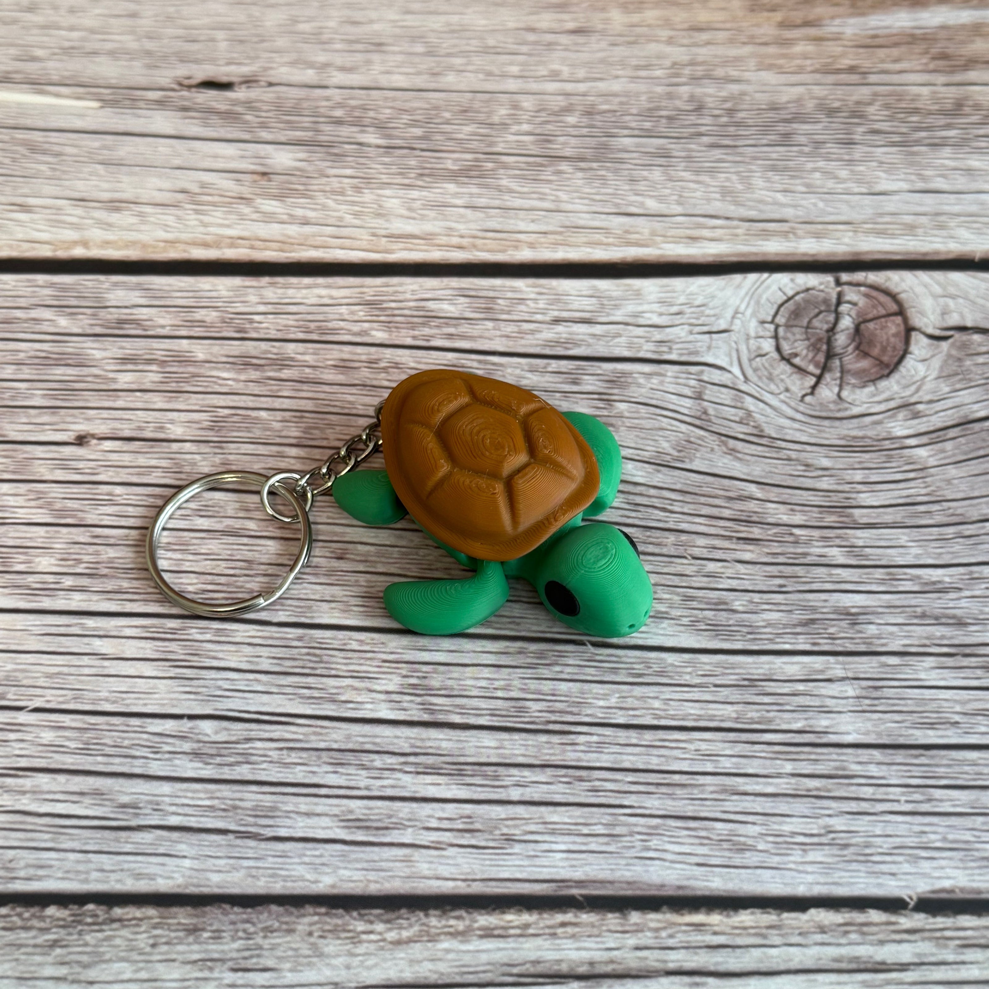 3D printed turtle-shaped keychain with brown shell and green body on a wooden surface