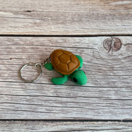 3D printed turtle-shaped keychain with brown shell and green body on a wooden surface