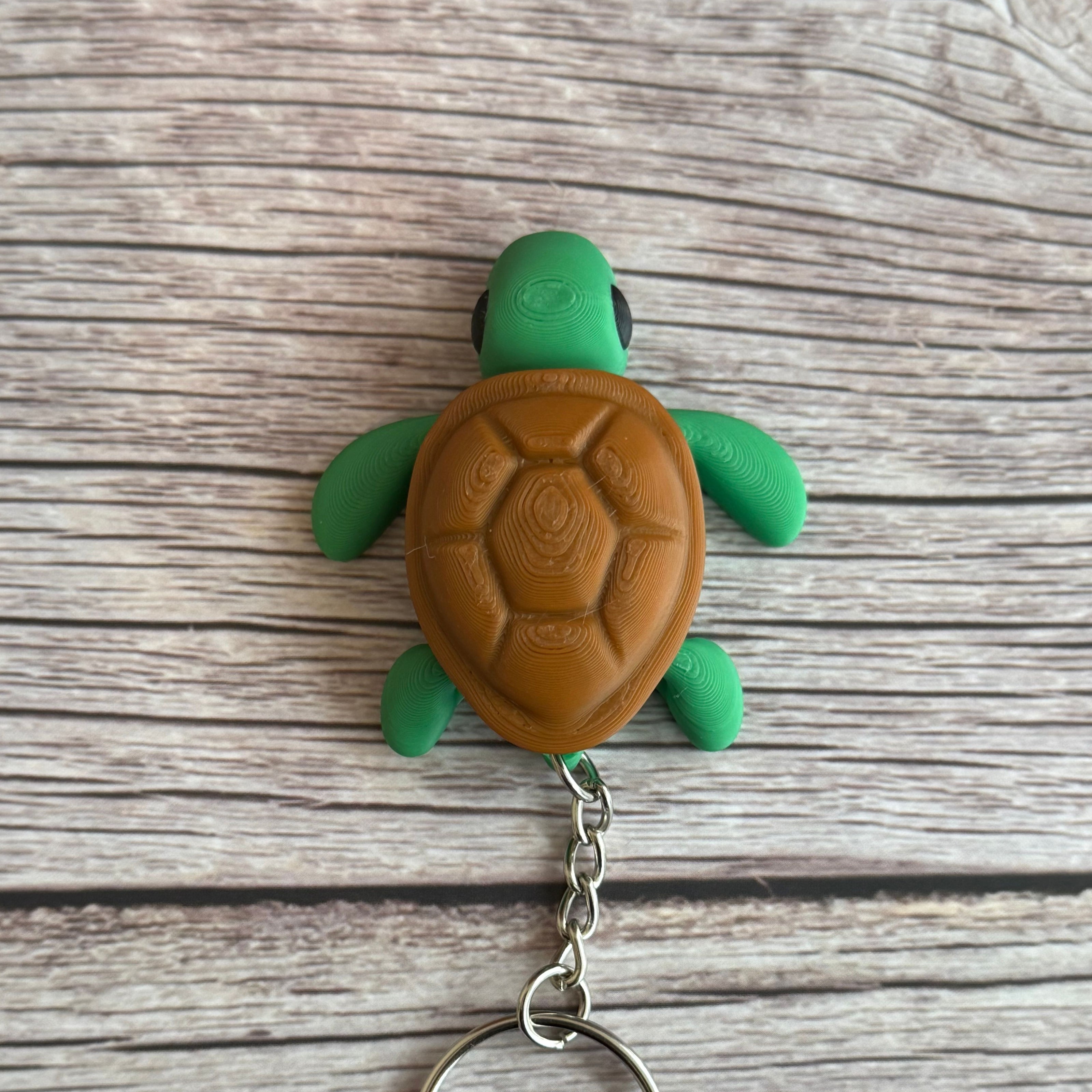 Top of a 3D printed turtle-shaped keychain with brown shell and green body on a wooden surface